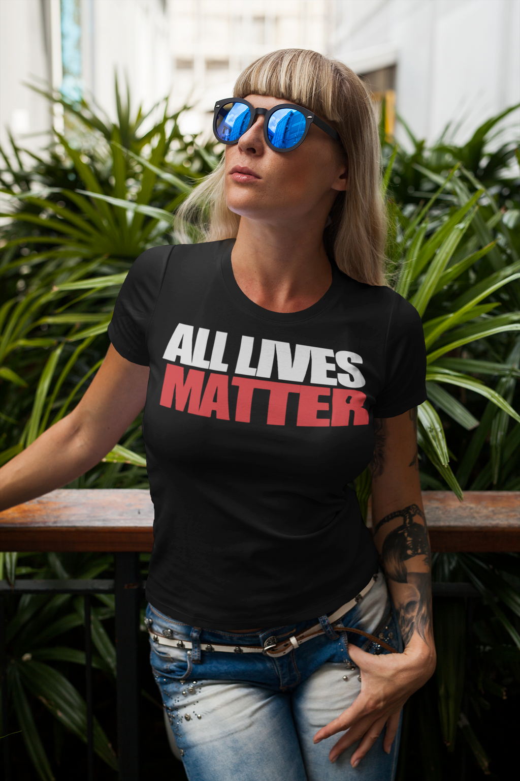 Woman wearing an Equality Matters Unity Graphic Tee with 'All Lives Matter' text, standing in front of lush greenery.