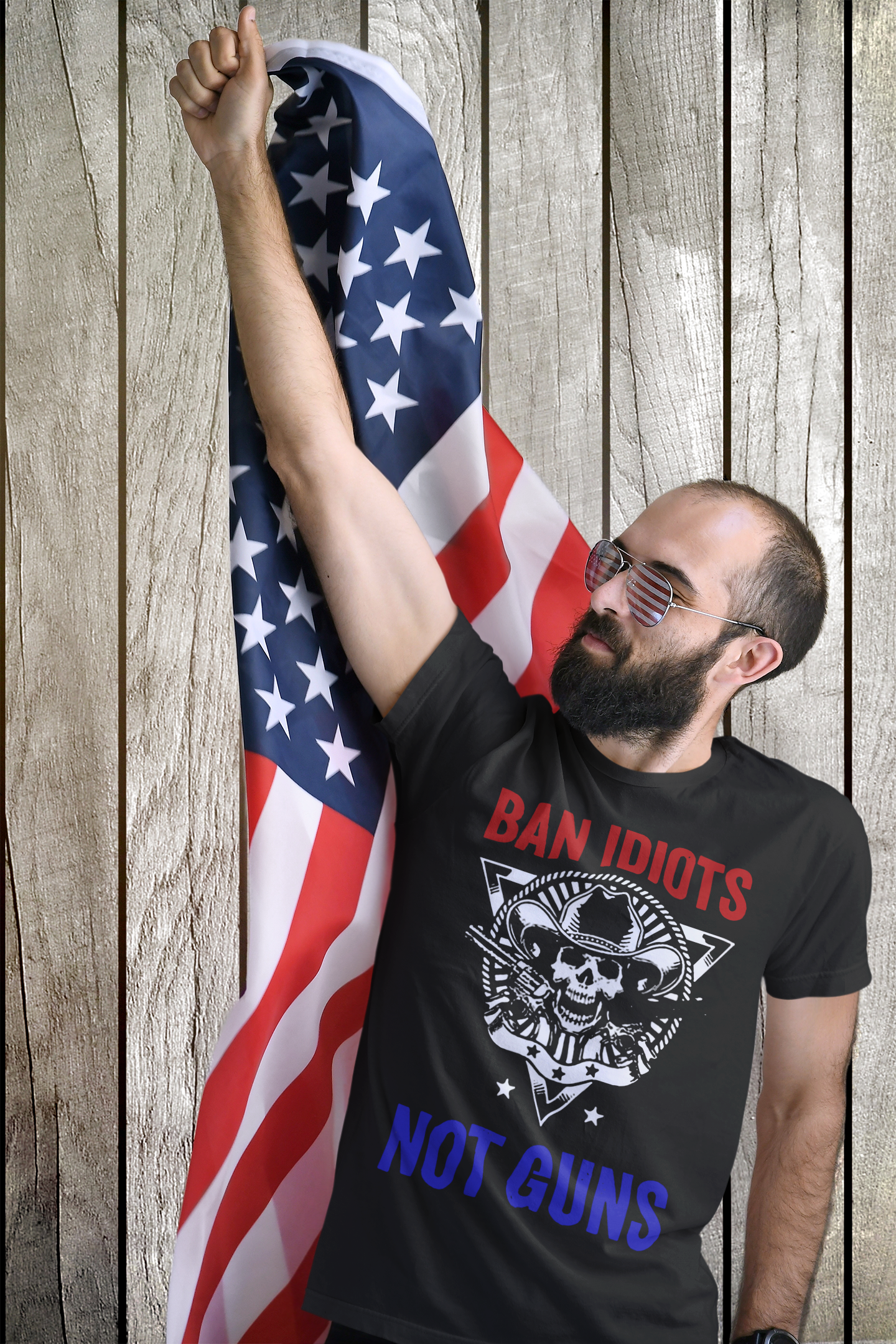 Man holding an American flag wearing a Ban Idiots Not Guns Custom Print t-shirt, promoting personal values.