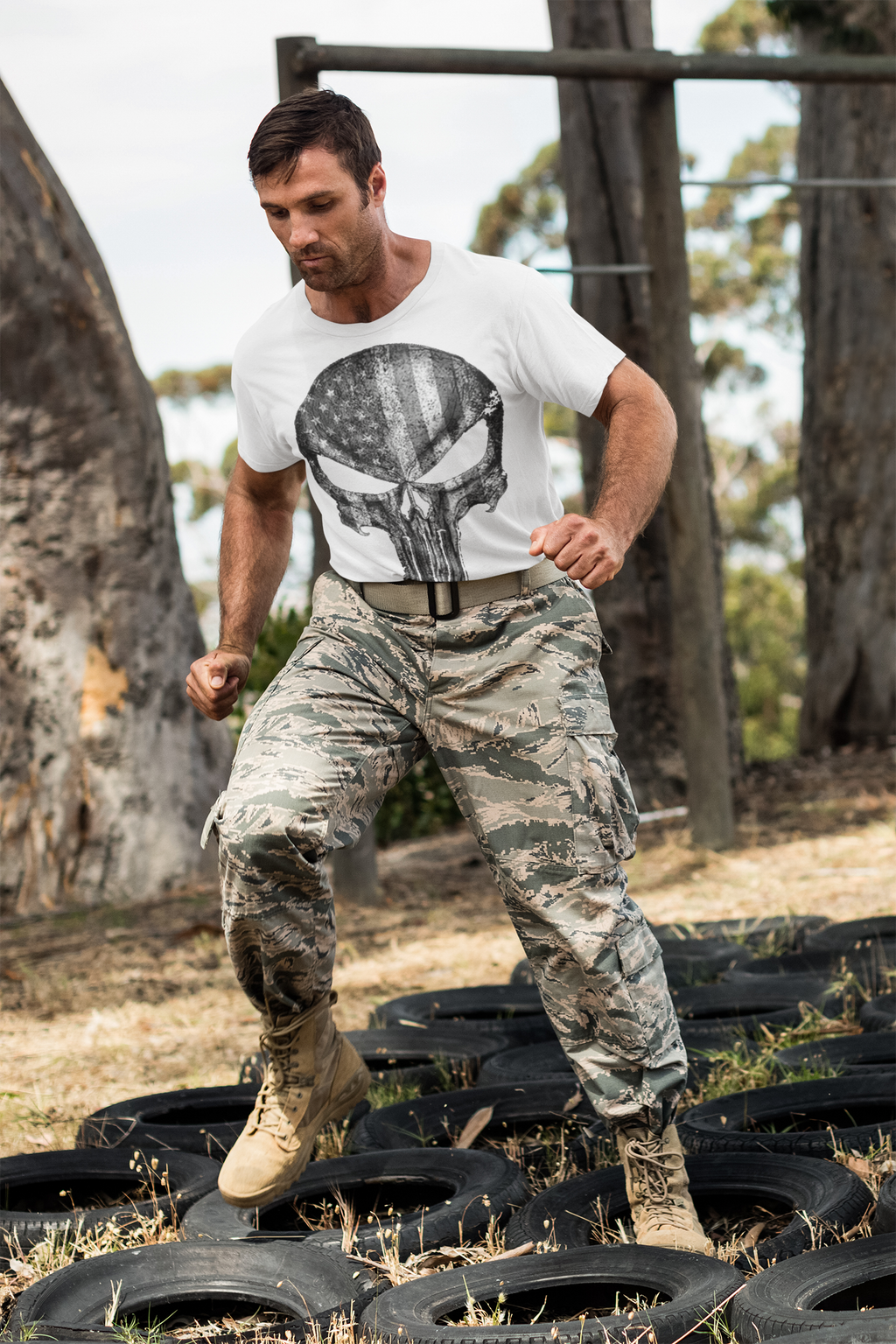 Man in camouflage pants and Punisher American Flag BW Graphic t-shirt training on tires outdoors.