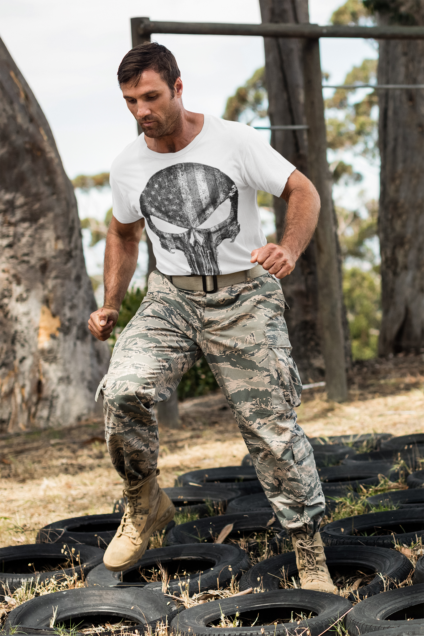Man in camouflage pants and Punisher American Flag BW Graphic t-shirt training on tires outdoors.