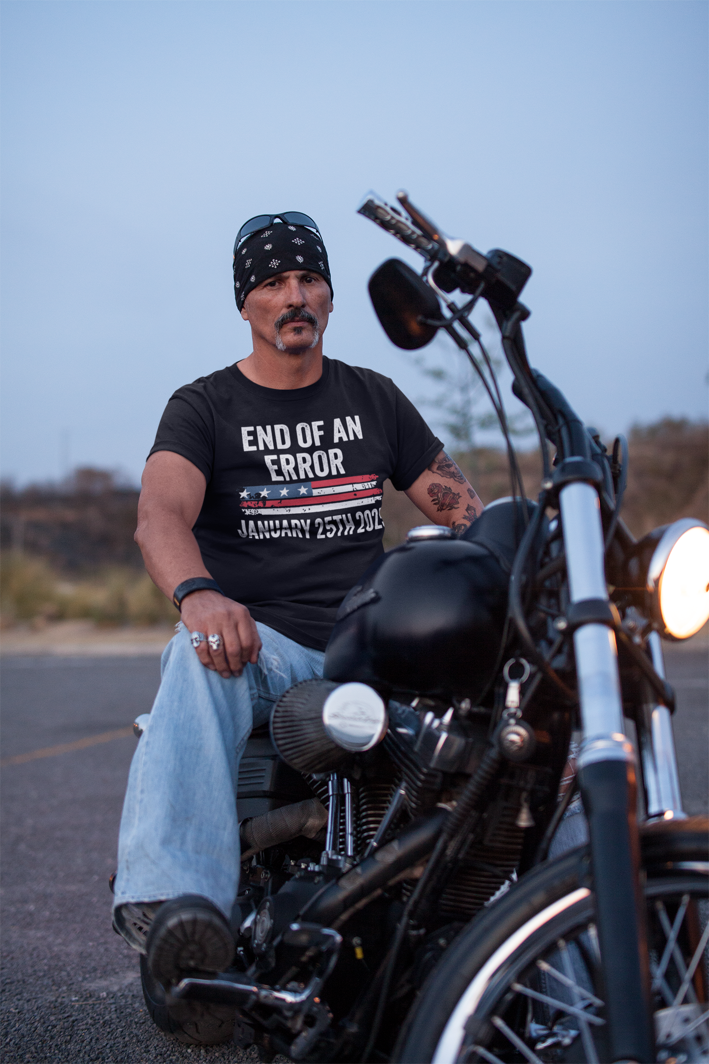 Man wearing Marking The End Of An Era Error t-shirt while sitting on a motorcycle at dusk.