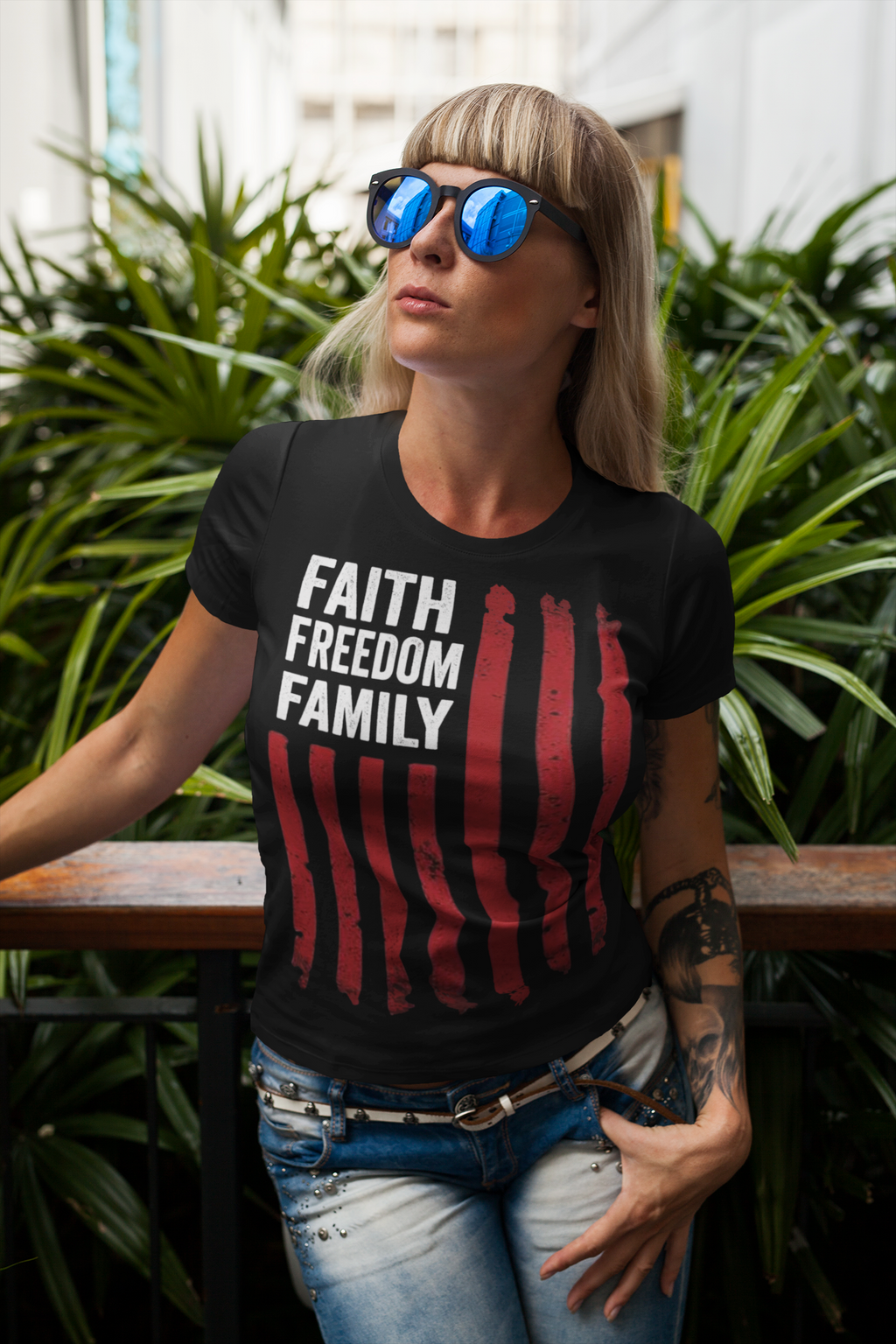 Faith Freedom Family Timeless Values Graphic T Shirt worn by a woman in shades, surrounded by greenery.
