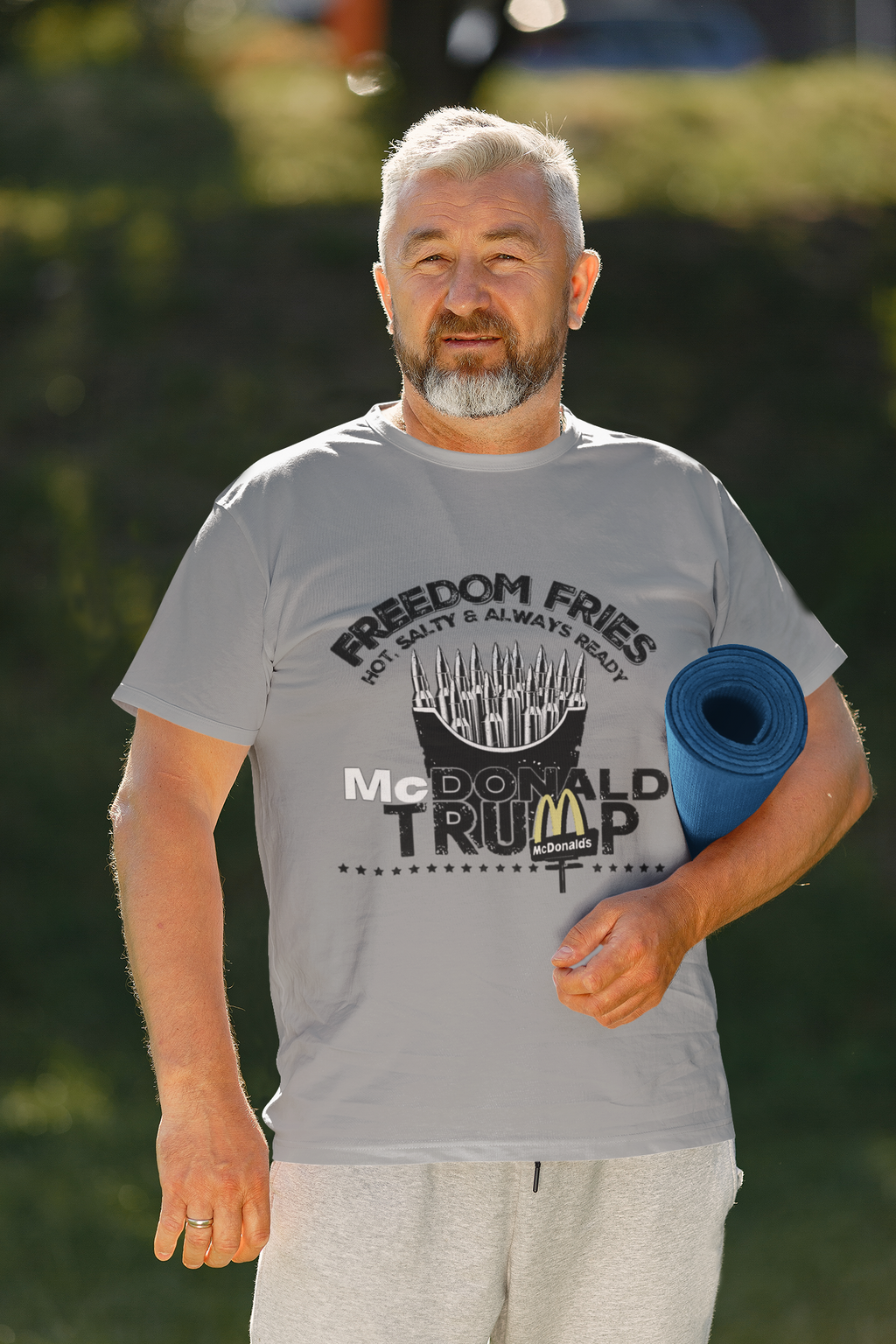 Man wearing Freedom Fries Custom Art Graphic t-shirt while holding a yoga mat in a sunny outdoor setting.
