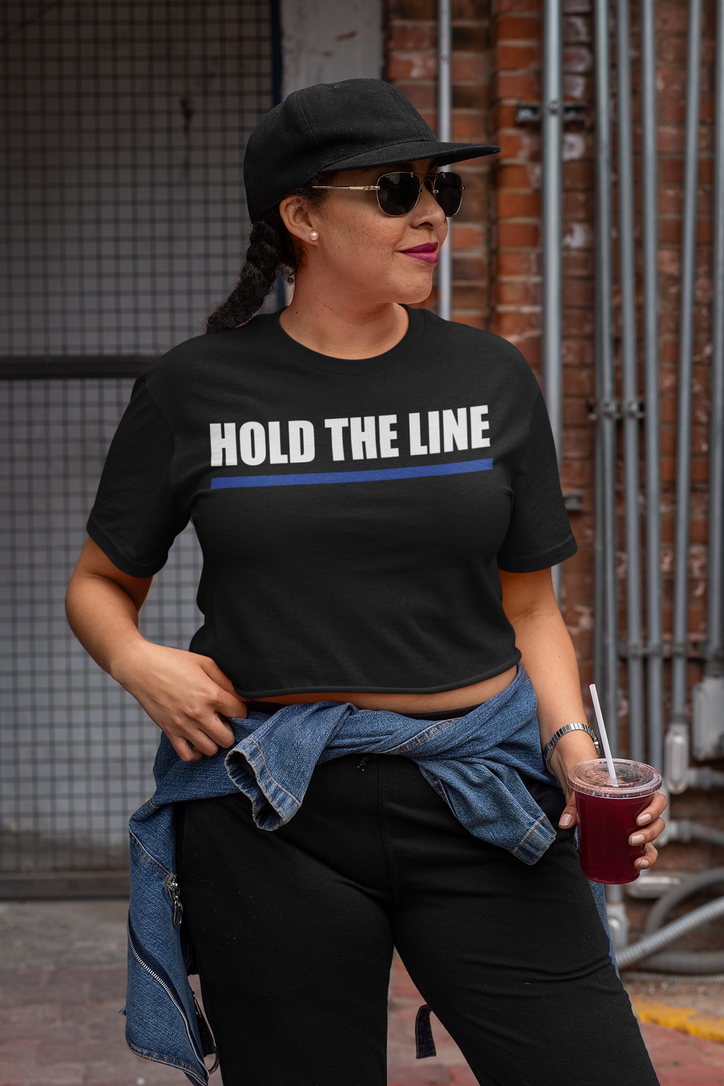 Hold The Line White Letters T Shirt worn by a woman in a stylish outfit with a drink, showcasing a bold message.
