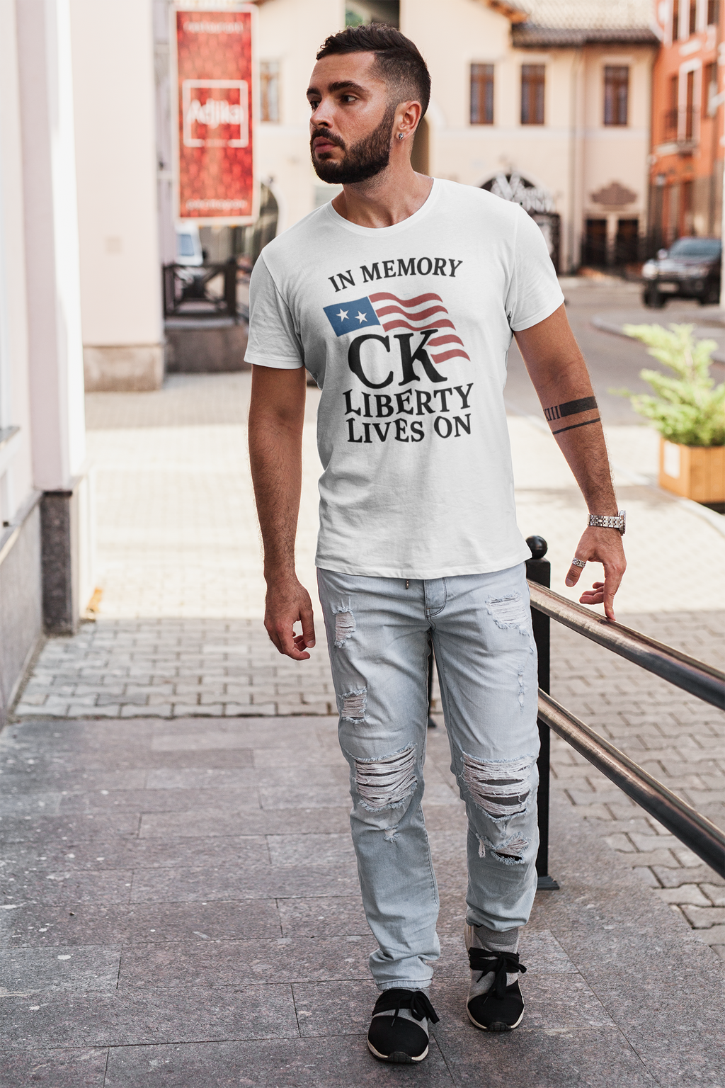 In Memory Of CK Charlie Kirk Liberty Lives On apparel worn by a man walking in a city street.