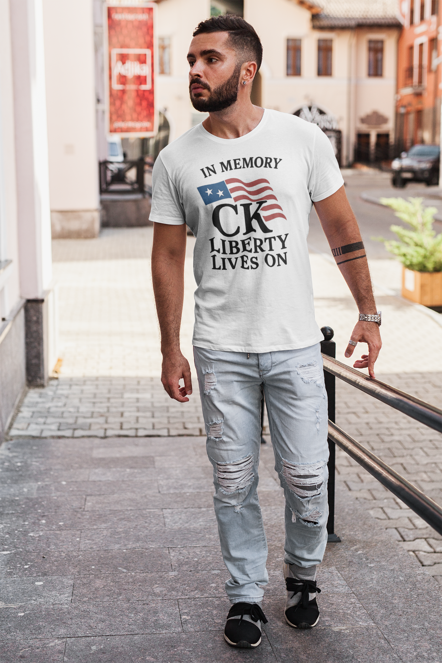 In Memory Of CK Charlie Kirk Liberty Lives On apparel worn by a man walking in a city street.
