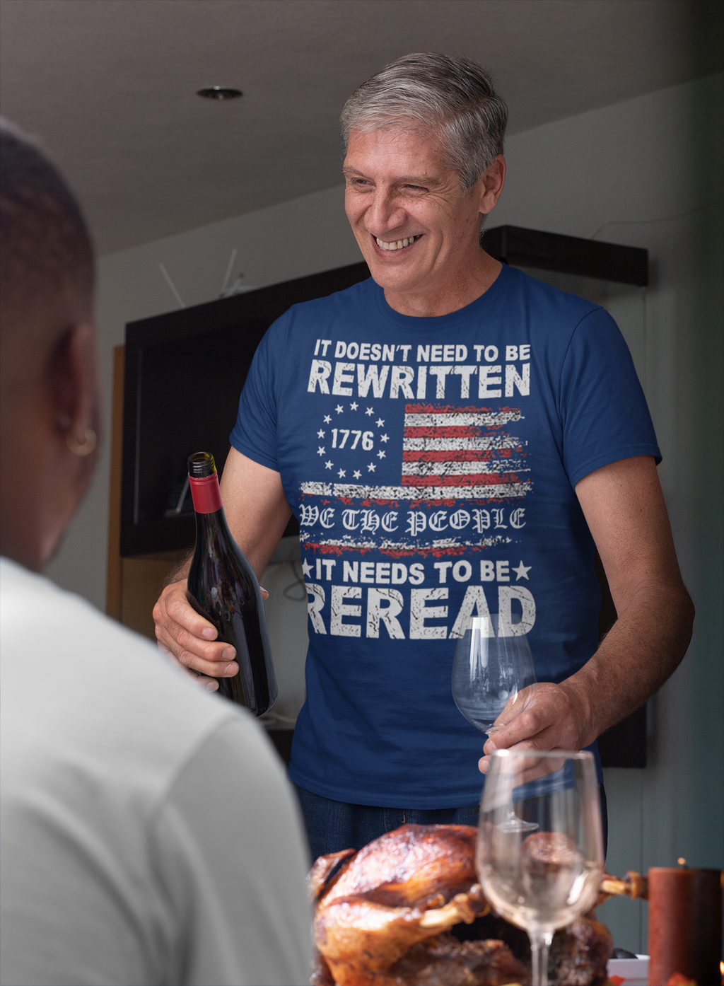 Man wearing It Needs to Be Reread Patriotic Design t-shirt while pouring wine at a dinner table.