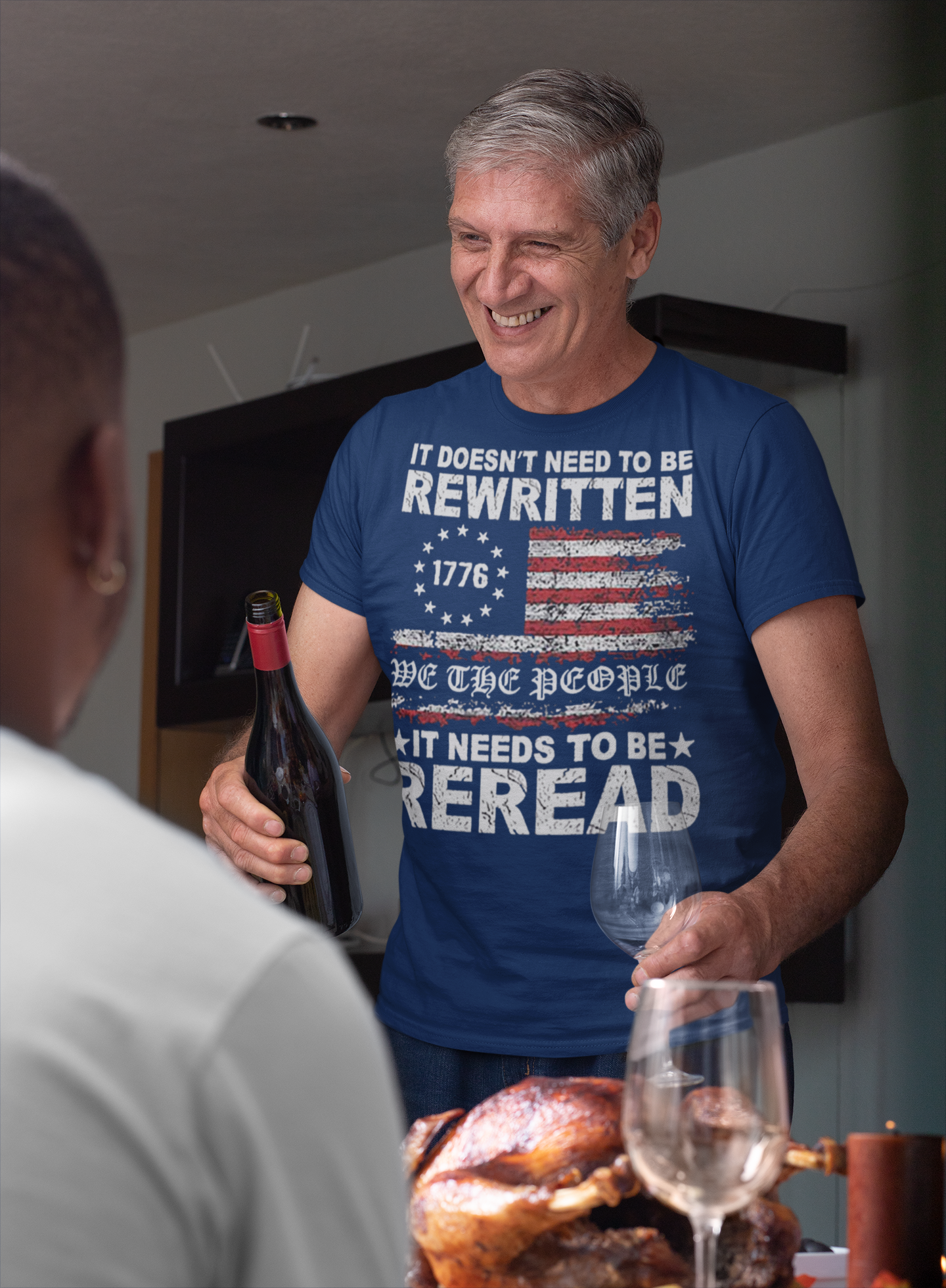 Man wearing It Needs to Be Reread Patriotic Design t-shirt while pouring wine at a dinner table.