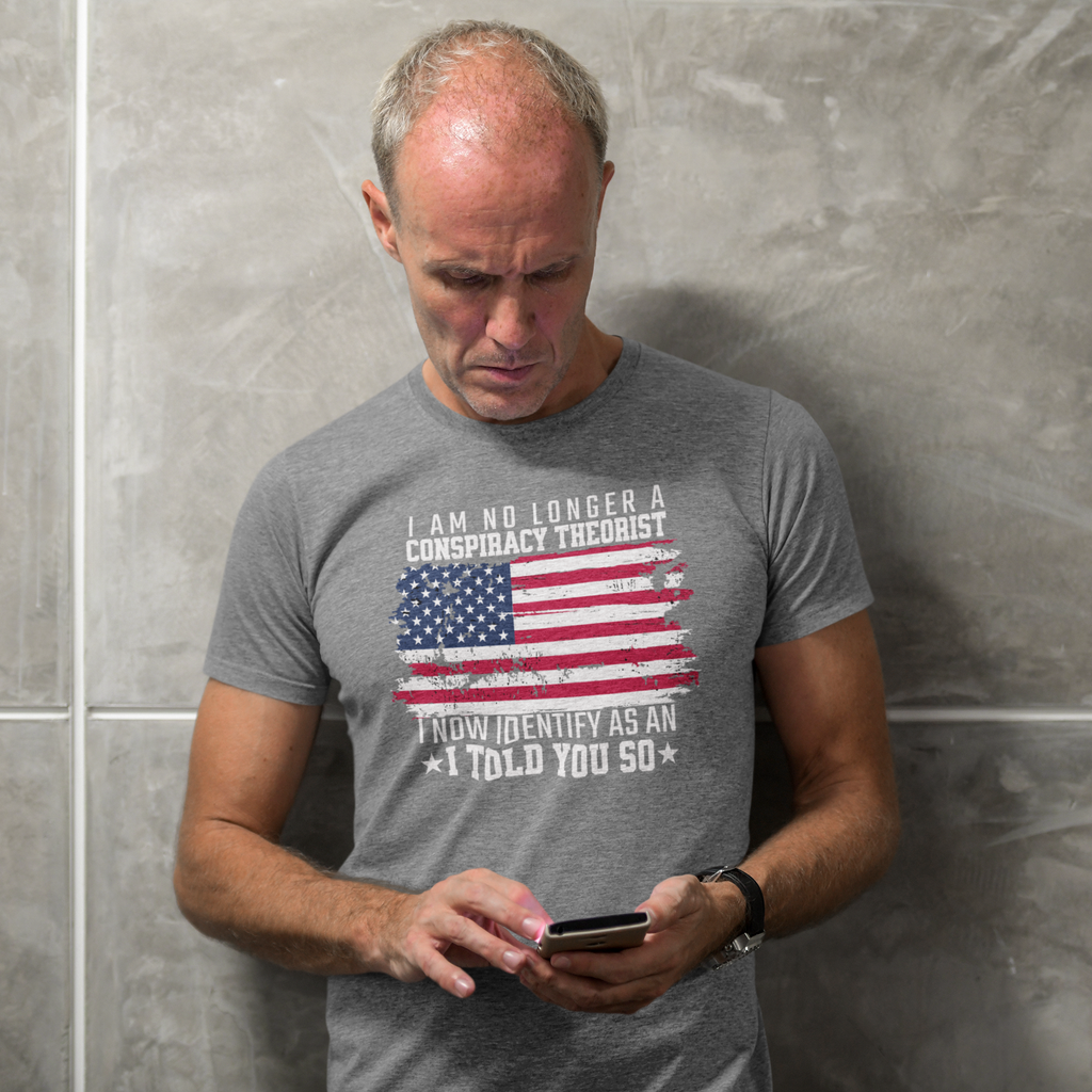 Man wearing I Am No Longer A Conspiracy Theorist t-shirt with American flag design, looking at his phone.