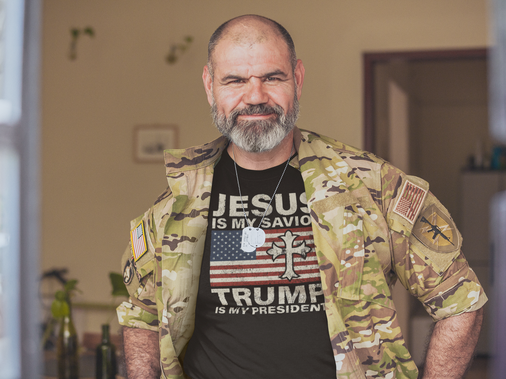 A man wearing a camo jacket and a t-shirt reading 'Jesus Is My Savior Trump Is My President'.