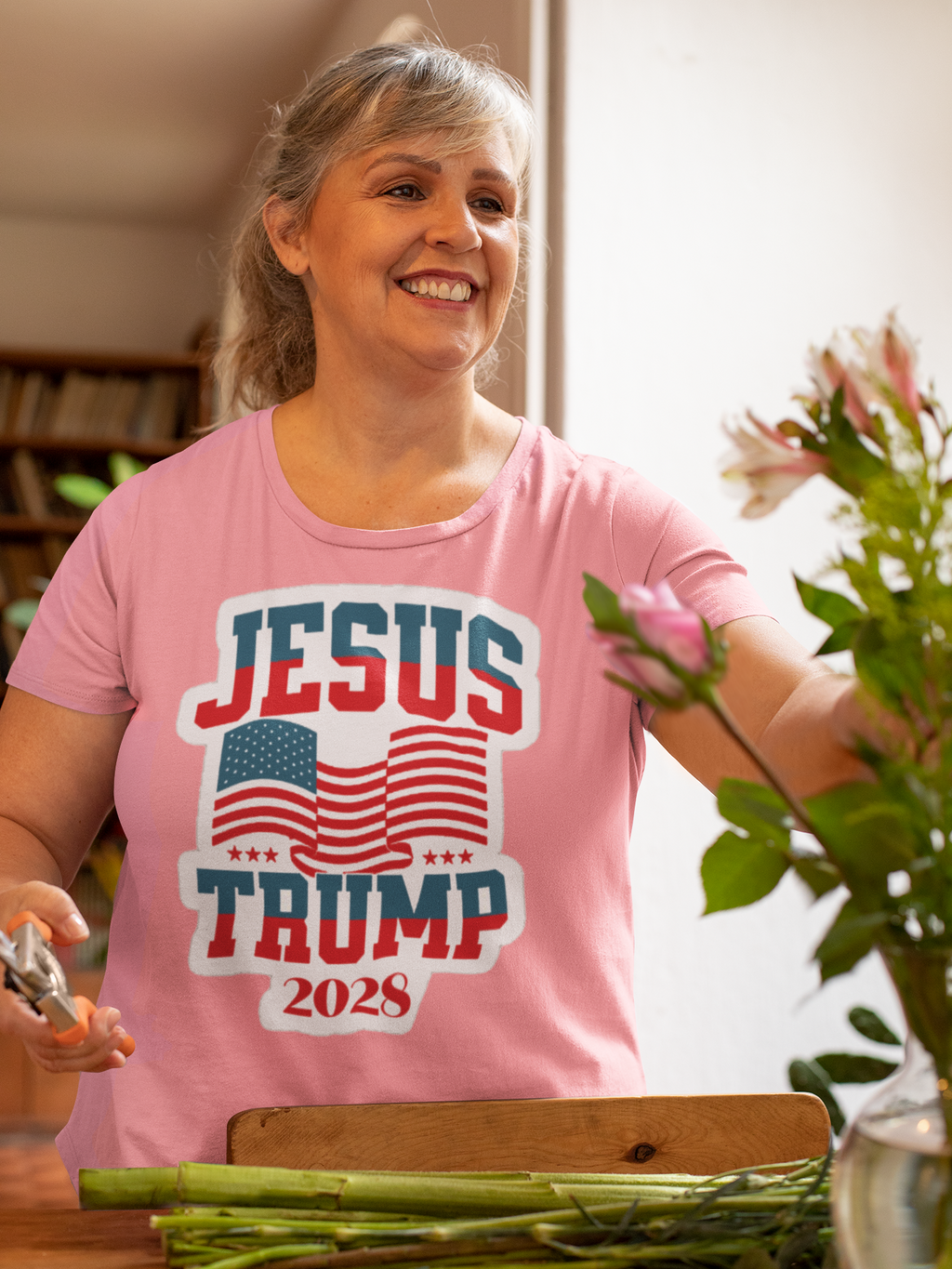 Smiling woman wearing JESUS TRUMP 2028 USA Patriotic Style t-shirt while arranging flowers.