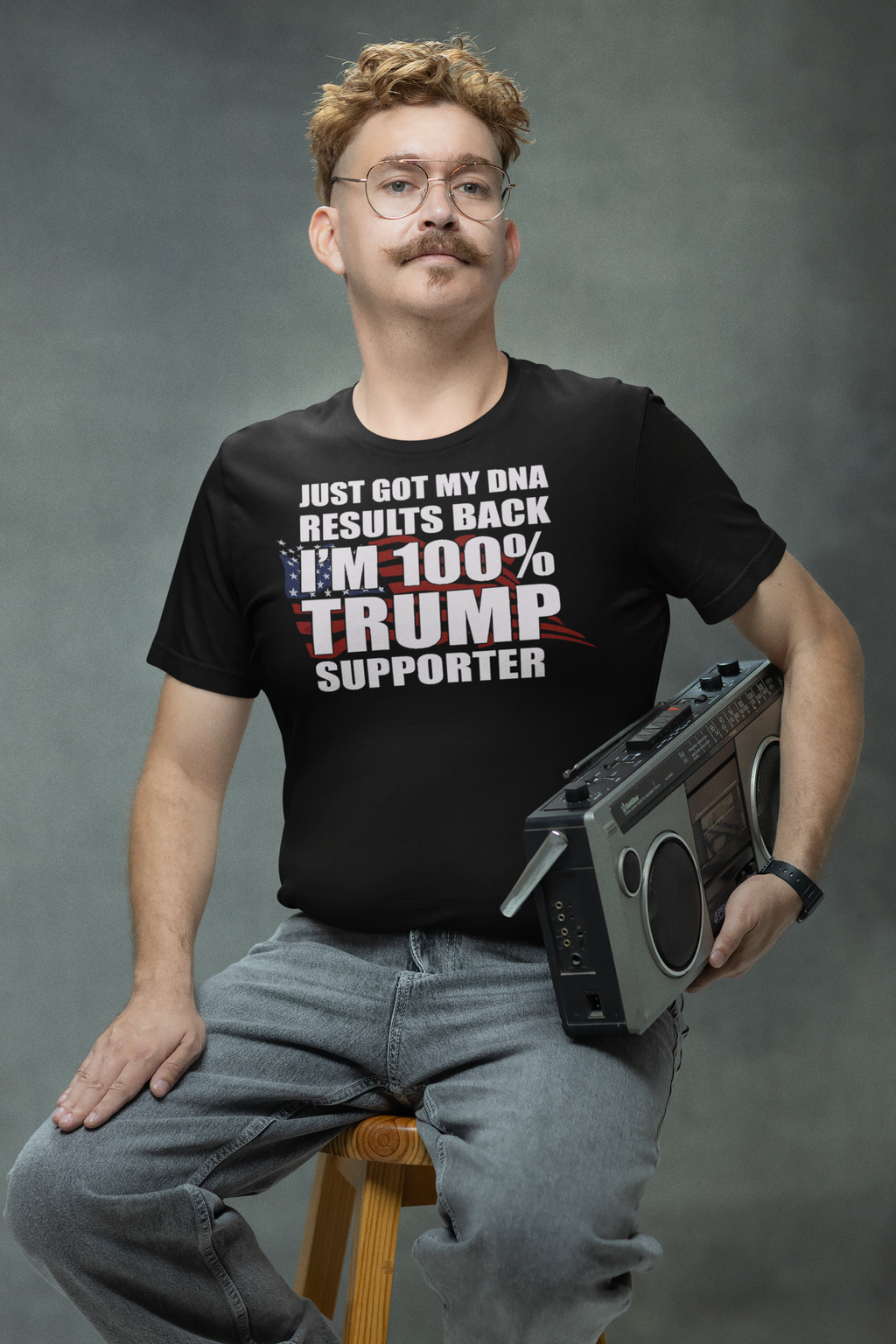 Man wearing 'DNA Results Back I Am One Hundred Percent Trump Supporter' shirt, sitting with boombox.