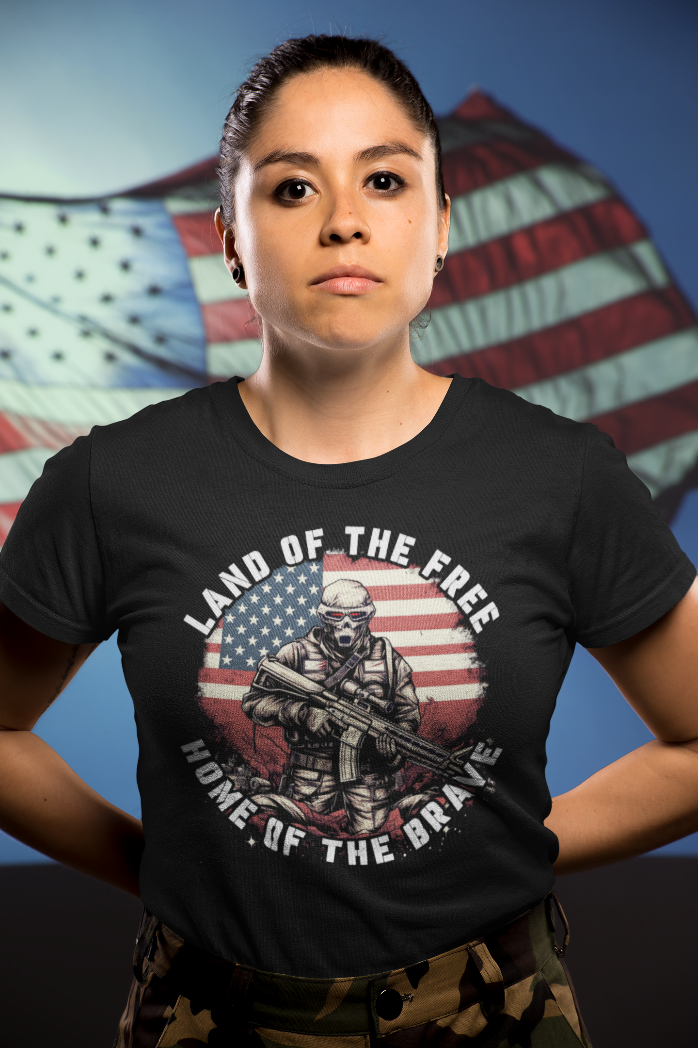 Woman wearing a Land Of The Free Home Of The Brave t-shirt with a soldier graphic, standing in front of an American flag.