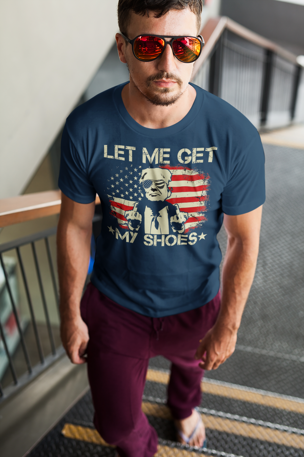 Man wearing Let Me Get My Shoes Statement Shirt with sunglasses on stairs, showcasing a bold design on a blue shirt.