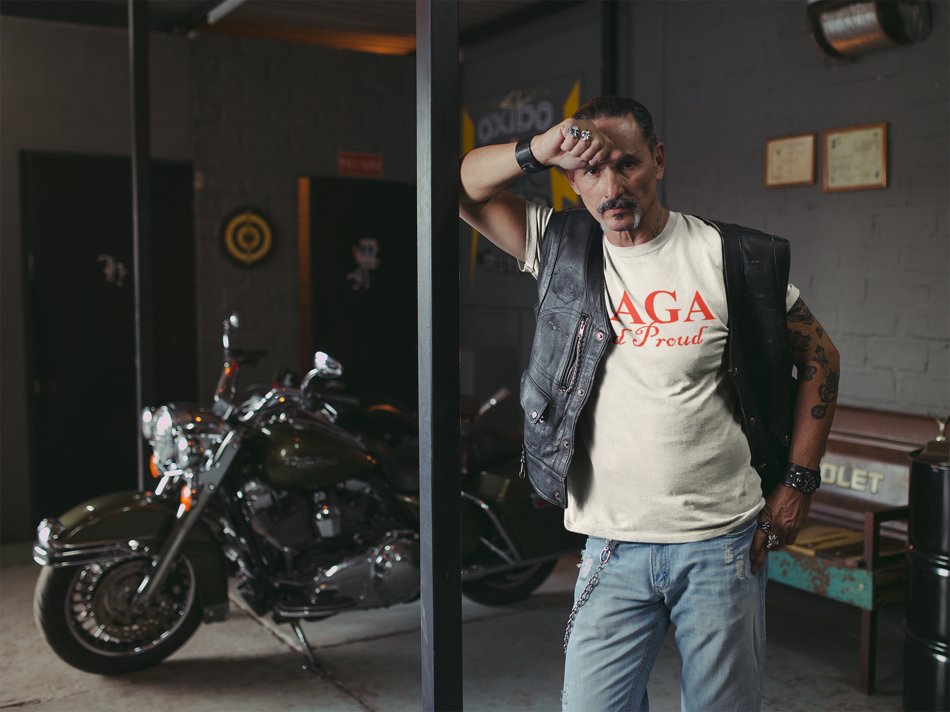Man wearing a MAGA And Proud Red Letters Style tee in a motorcycle garage setting.