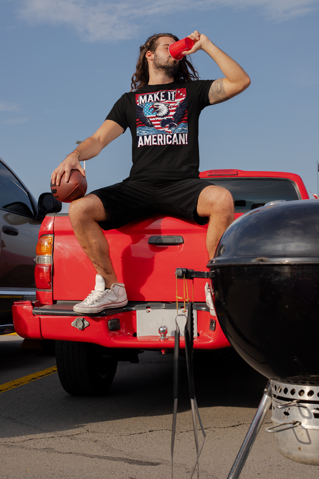 Man wearing Make It American American Pride Shirt, sitting on truck tailgate, enjoying beverage, showcasing patriotism.