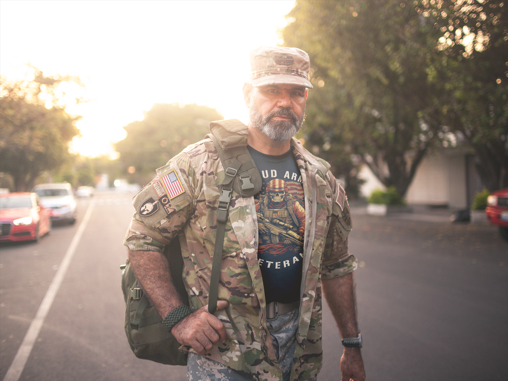 Proud Army Veteran Graphic Tee worn by a soldier in military gear walking down a street at sunset.
