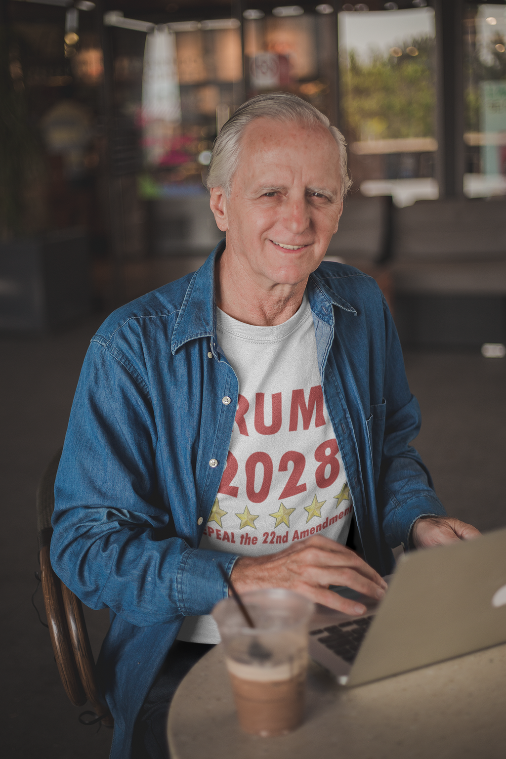 Man wearing a Trump 2028 t-shirt advocating for the 2028 Repeal 22nd Amendment Trump while using a laptop.