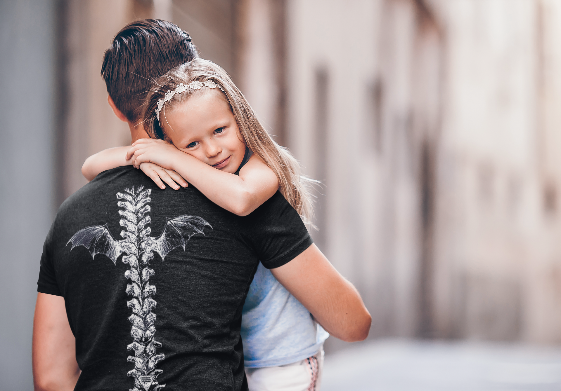 Child hugging a person wearing a Winged Spine Back Graphic Print t-shirt in a casual setting.