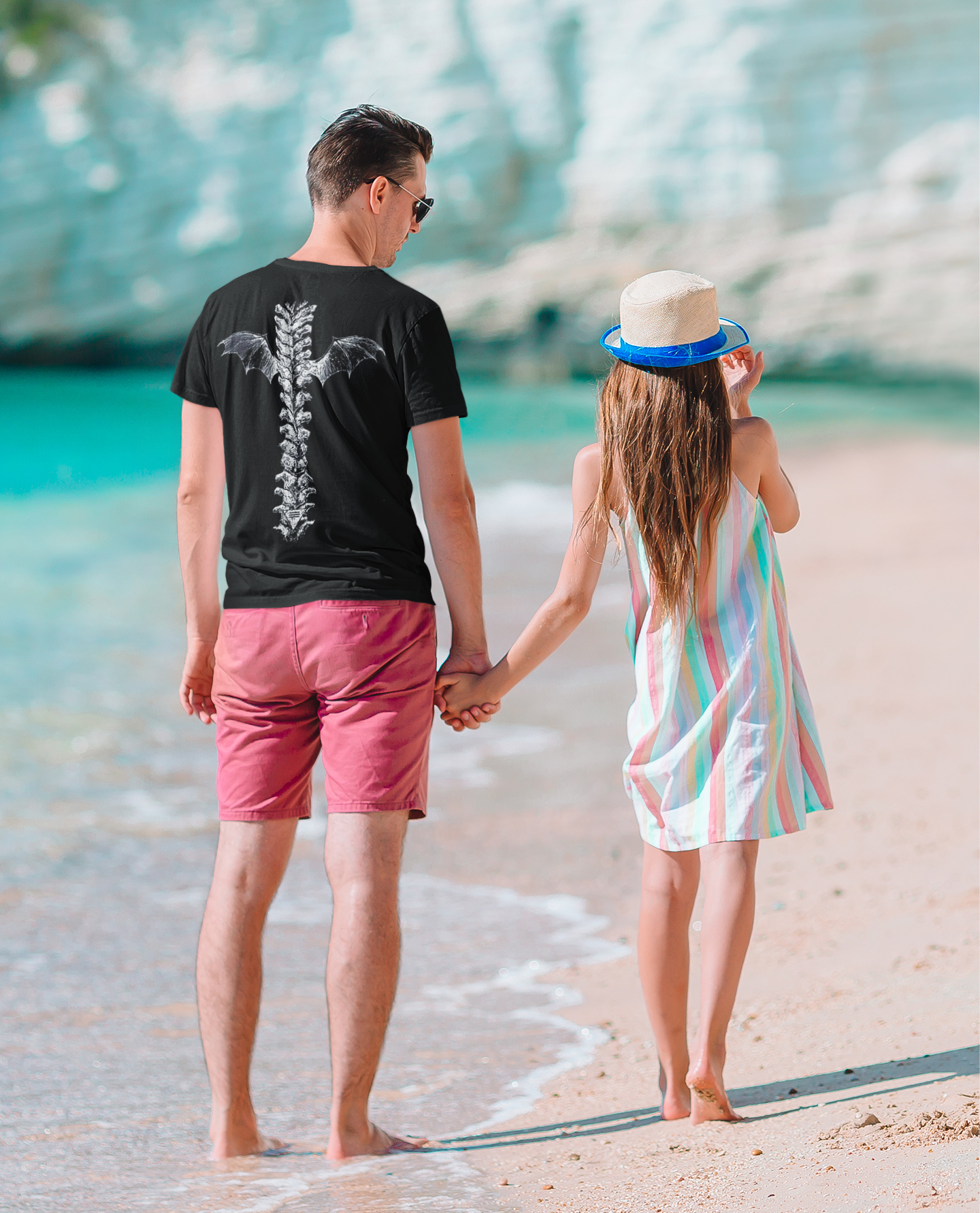 Couple walking on beach, wearing Winged Spine Back Graphic Print t-shirt and enjoying the sunny day.