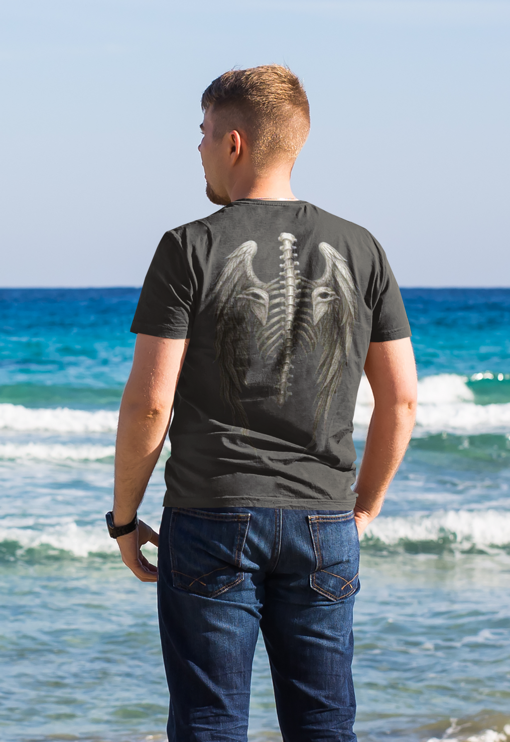 Spine Eagle Wings Back Print Tee worn by a man at the beach with ocean waves in the background.