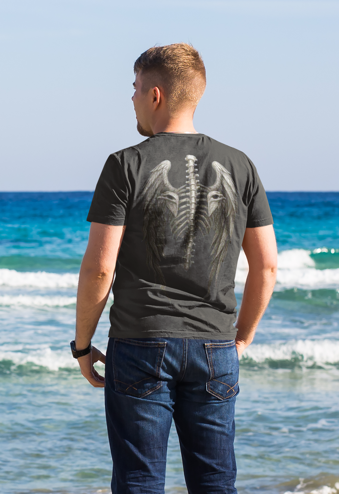 Spine Eagle Wings Back Print Tee worn by a man at the beach with ocean waves in the background.