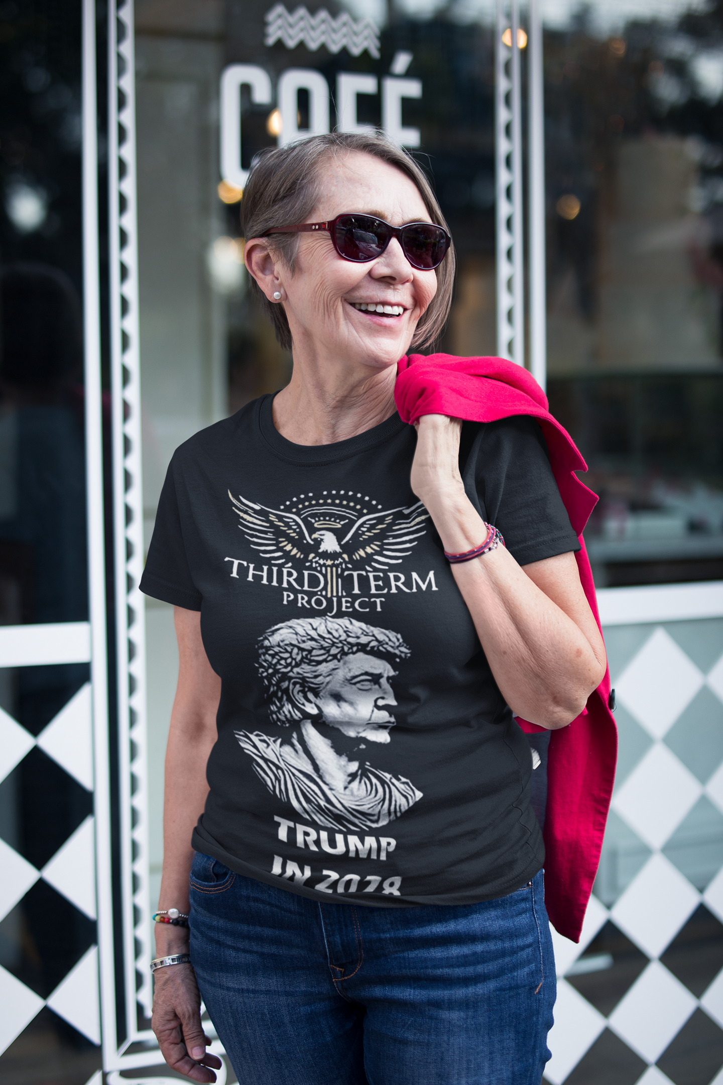 Woman wearing a Third Term Project Trump 2028 Graphic t-shirt outside a café, smiling and stylish.