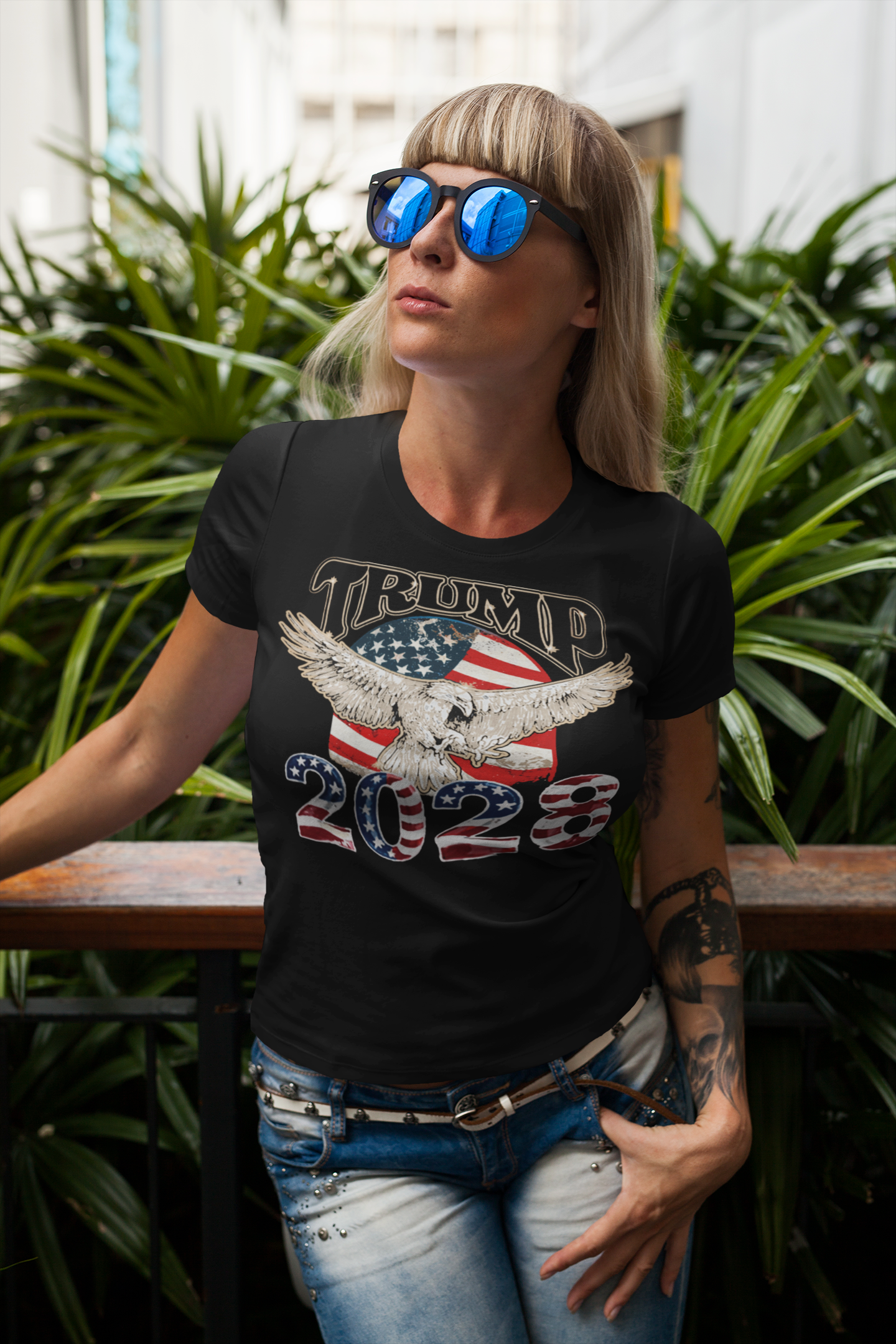 Trump 2028 On USA Flag And Eagle apparel worn by a woman in sunglasses amidst greenery.