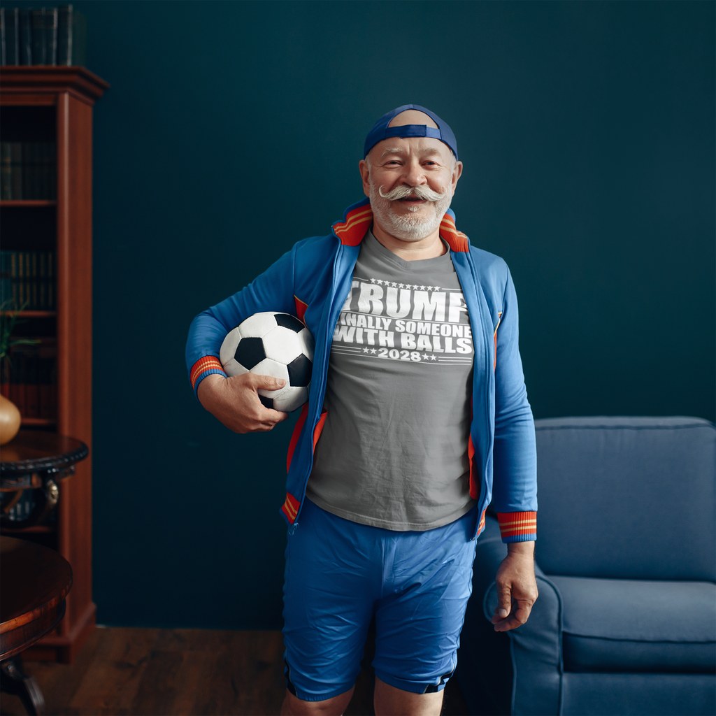 Man wearing Trump 2028 Finally Someone With Balls shirt holding a soccer ball in a cozy room.