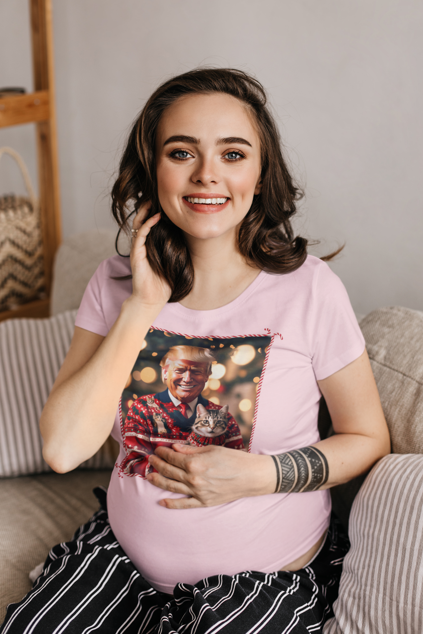Smiling pregnant woman in a pink Trump Christmas Sweater For Cat Lovers, holding a cat and sitting on a couch.