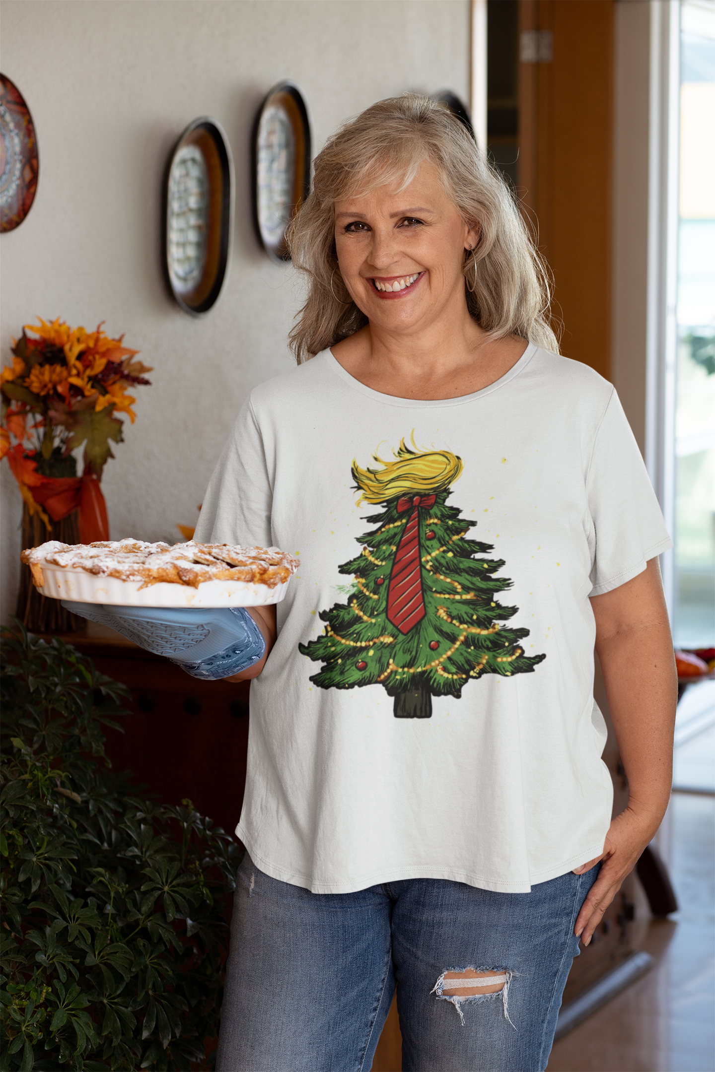Woman wearing Trump Christmas Tree Decor Item shirt while holding a pie in a festive home setting.