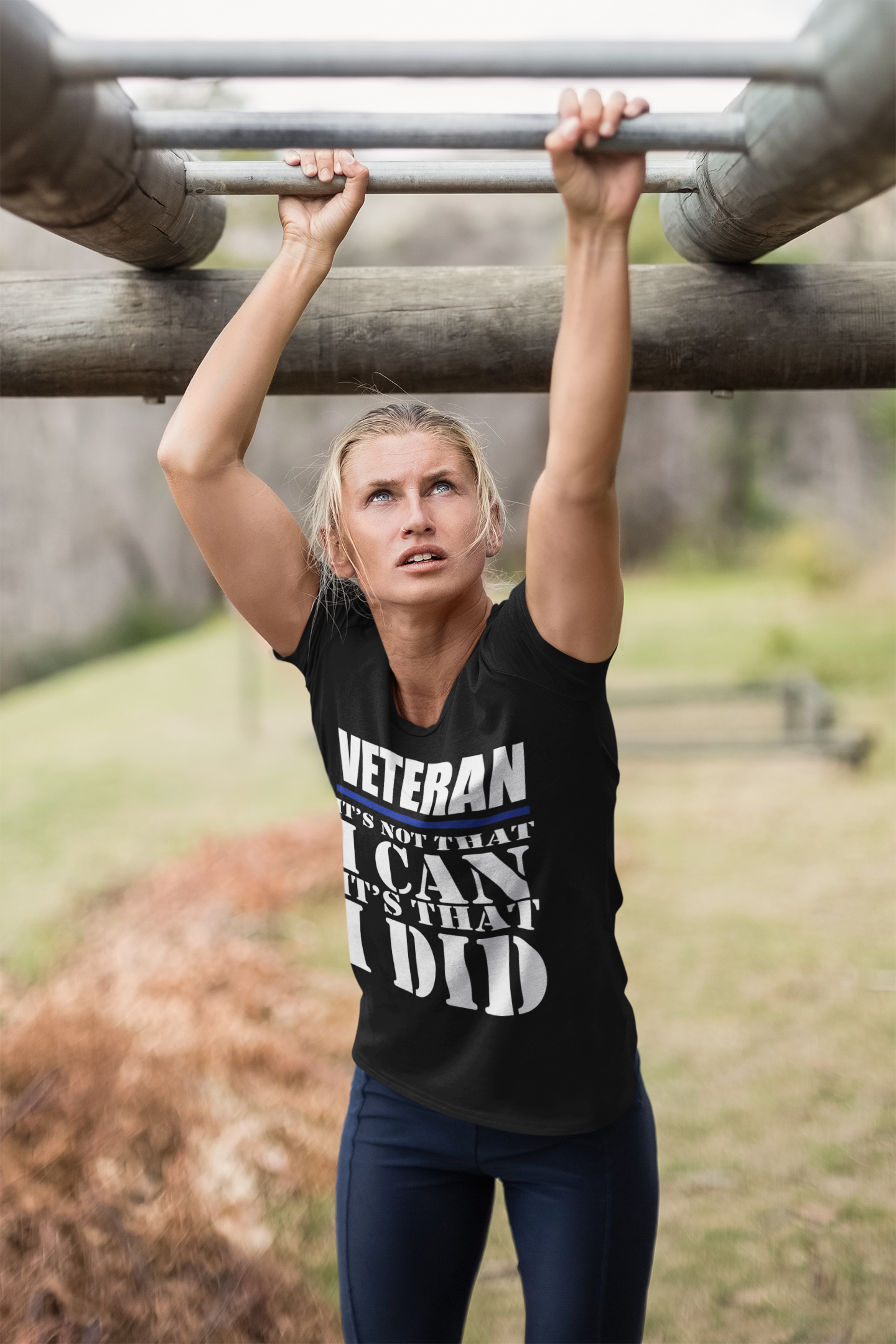 Woman in a black shirt with the phrase 'Veteran It Is That I Did Design' working out on a fitness obstacle.