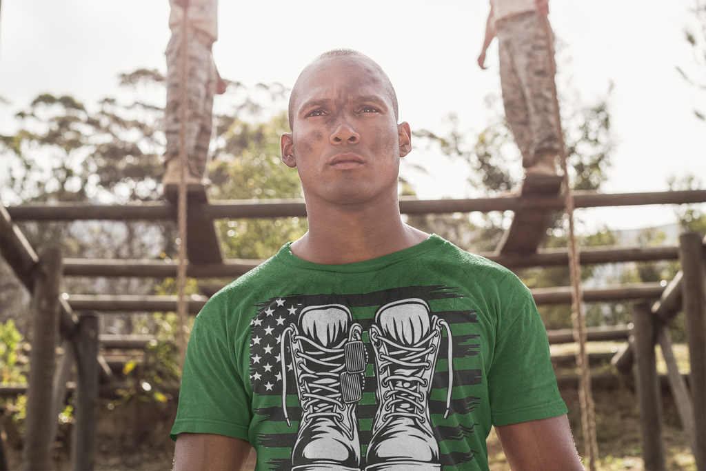 Man wearing Walk A Mile In Mine Apparel Art shirt with military boots design, outdoors, showing support for national ideals.