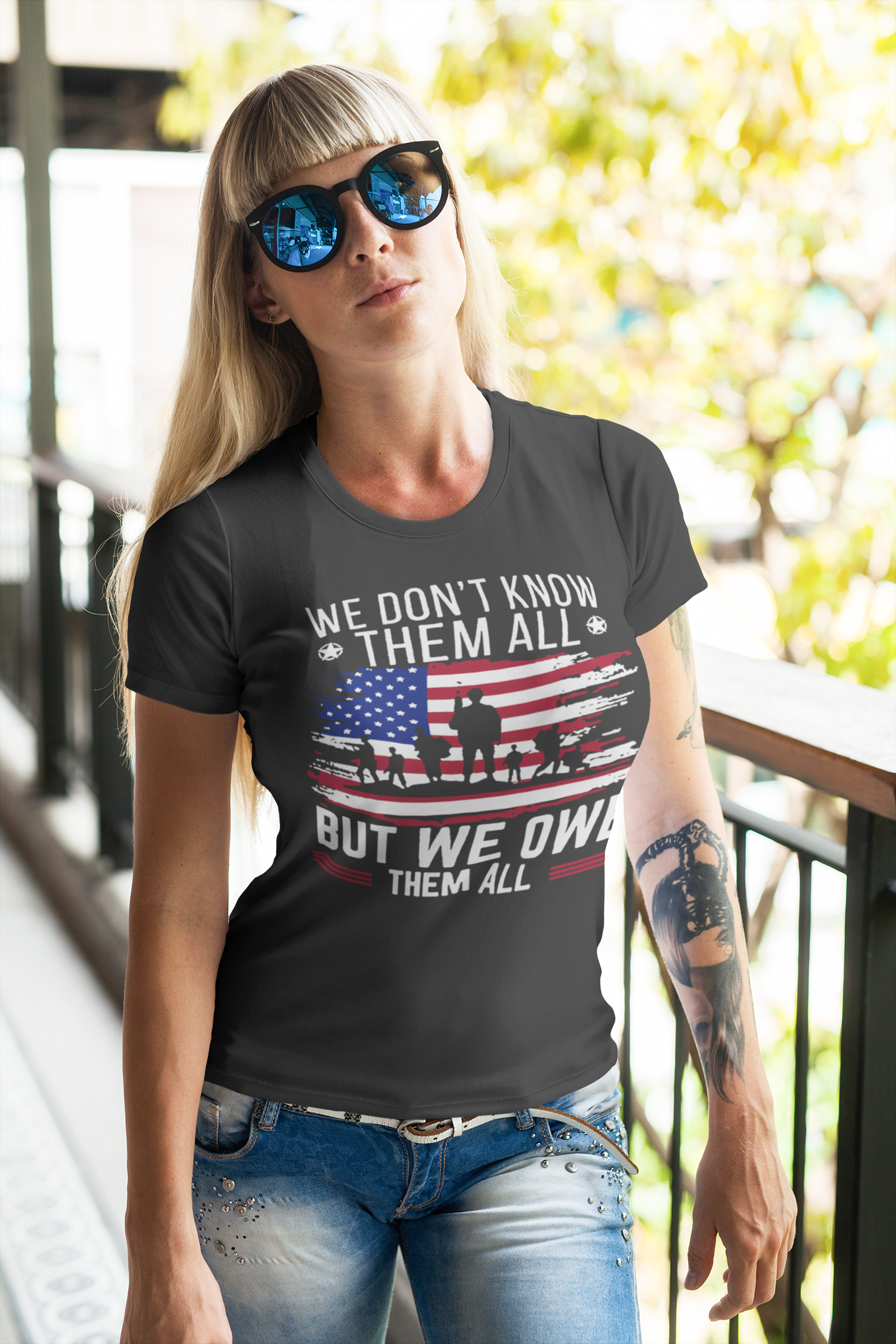 Woman wearing a shirt with We Don't Know Them All But We Owe Them All On American Flag design, celebrating patriotism.