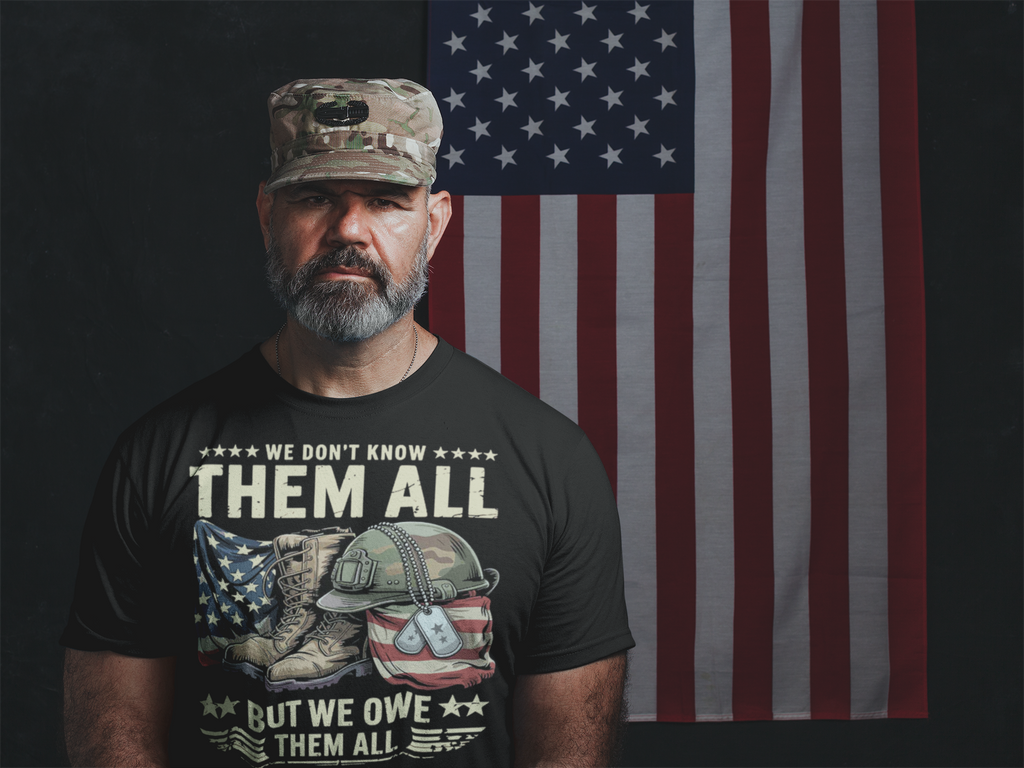 Man wearing a shirt with the phrase 'We Don't Know Them All But We Owe Them All' in front of an American flag.