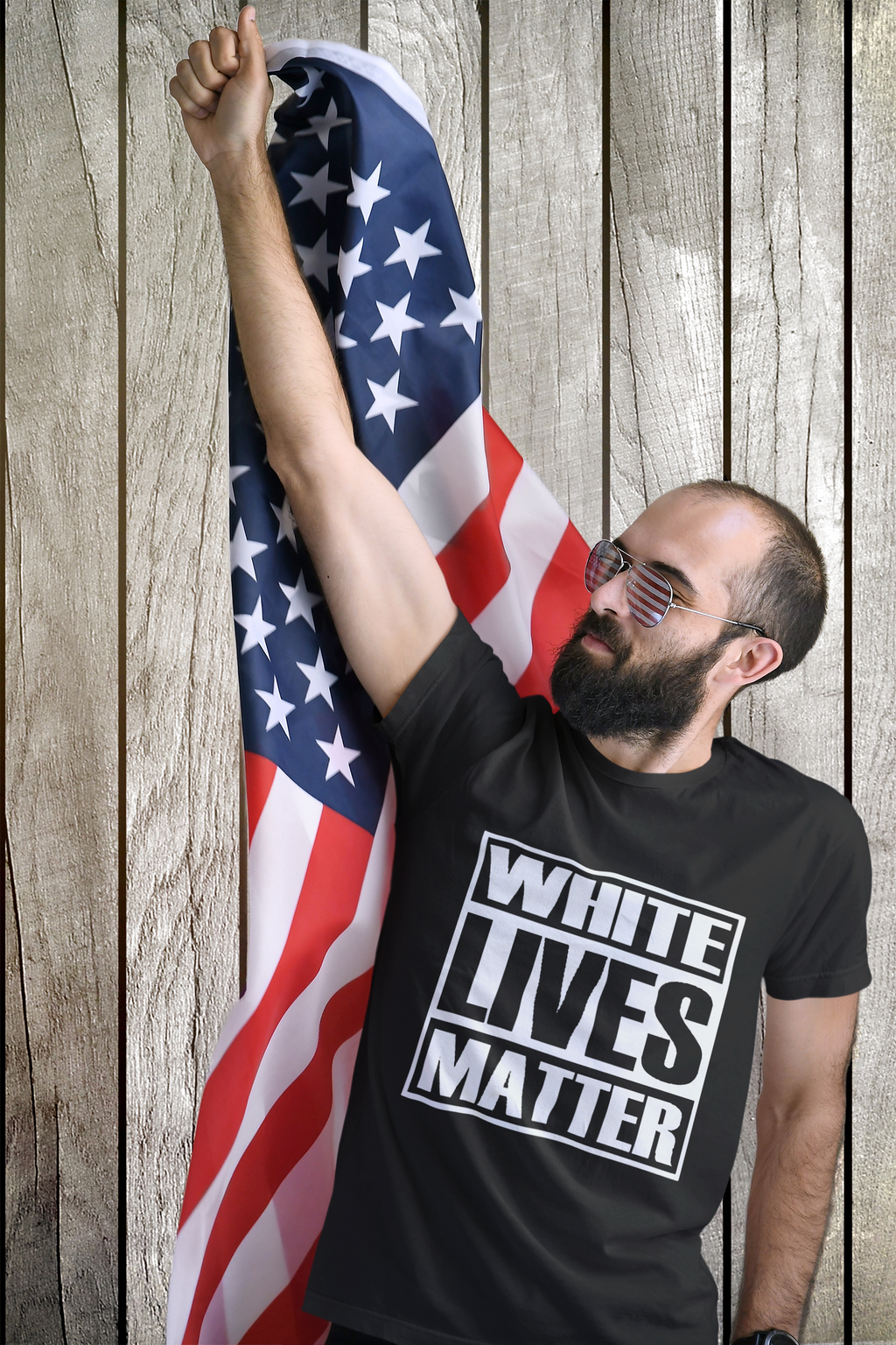 Man wearing Unity Matters Black & White Graphic Shirt holding American flag in front of wooden wall.