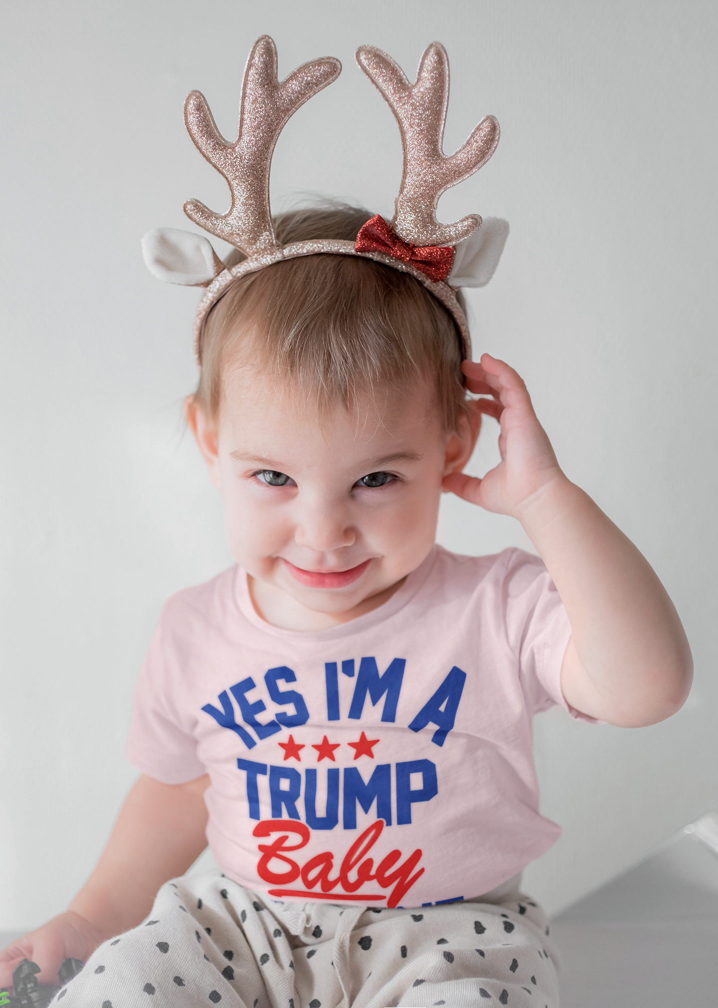 Toddler wearing a Trump Baby Get Over It Kids Tee with festive antlers, smiling joyfully.