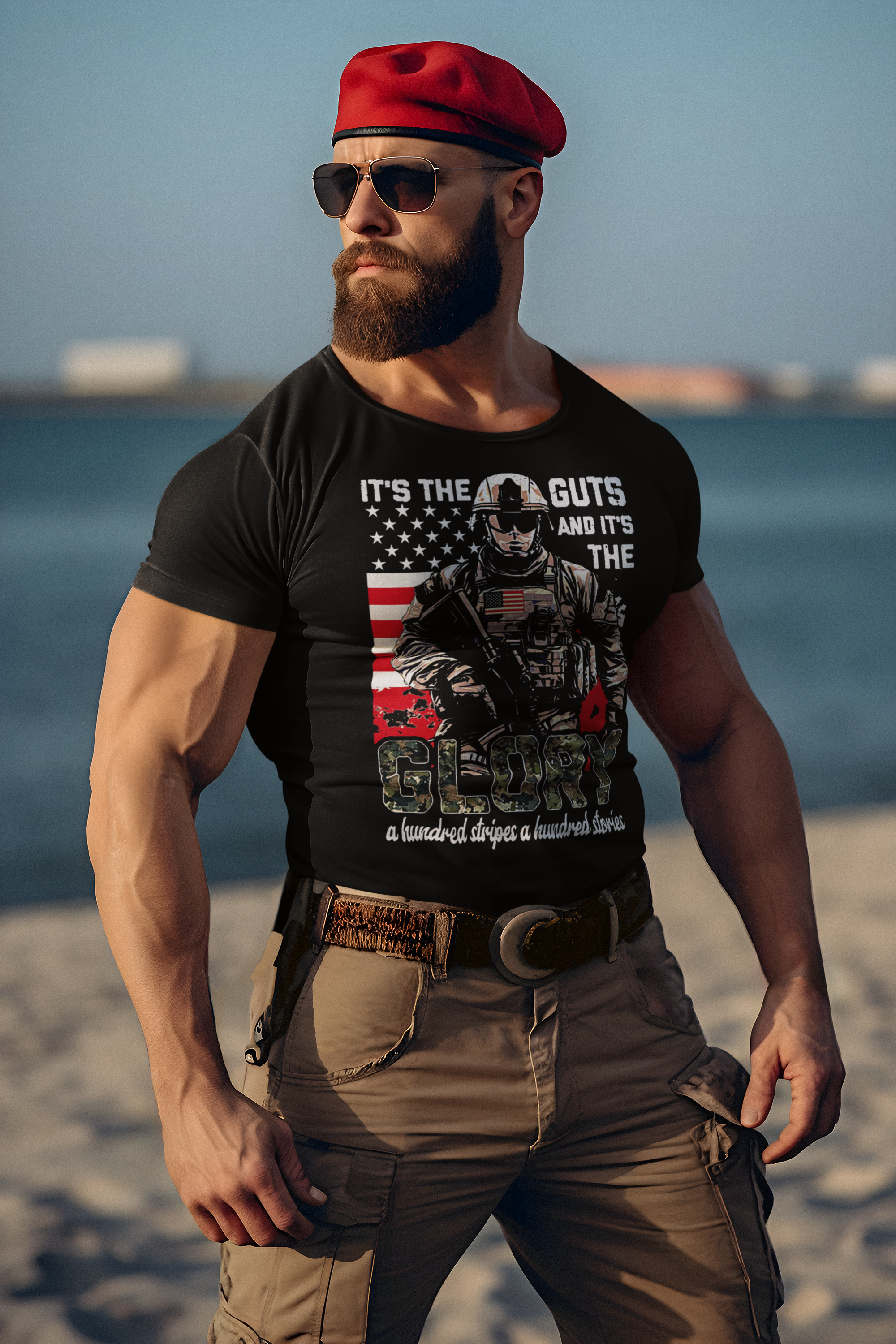 A muscular man wearing a black t-shirt that reads "It's The Guts And It's The Glory" at the beach.