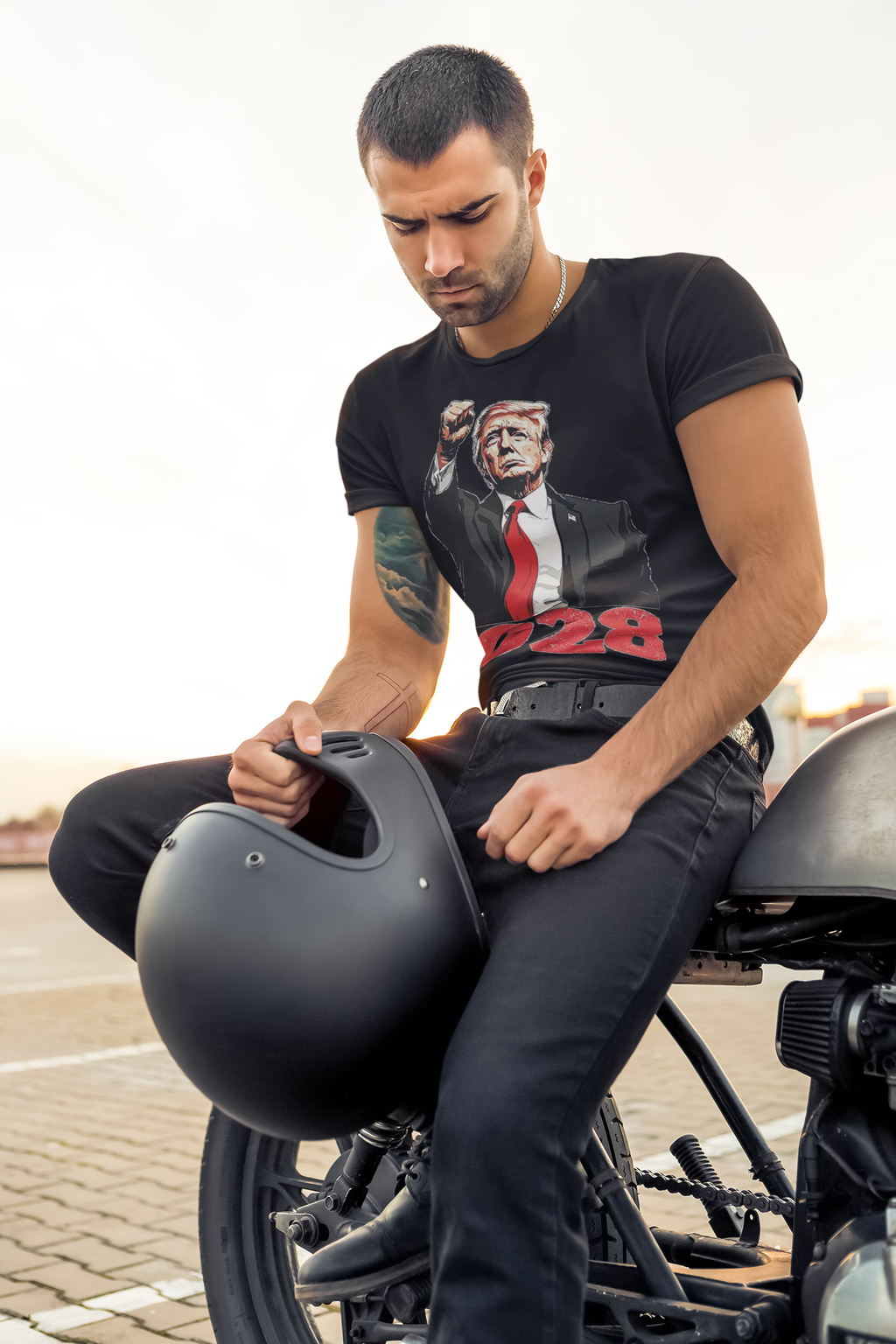 Man wearing Bold Trump 2028 Fist Art Apparel tee while sitting on a motorcycle, holding a black helmet.