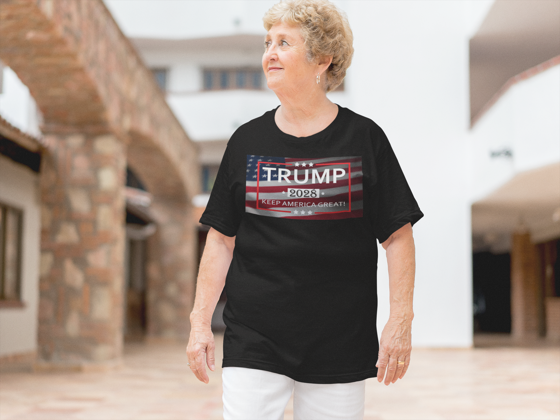 Woman wearing a black t-shirt featuring the Keep America Great 2028 Design and Trump 2023 graphic, in a sunny courtyard.