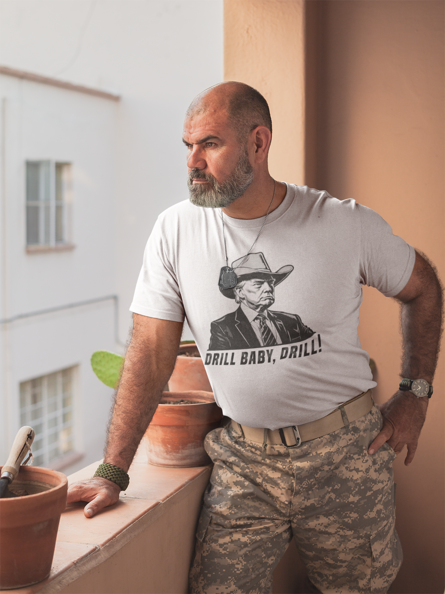 Man wearing a Drill Baby Drill Bold Graphic Tee with a strong expression, standing on a balcony.