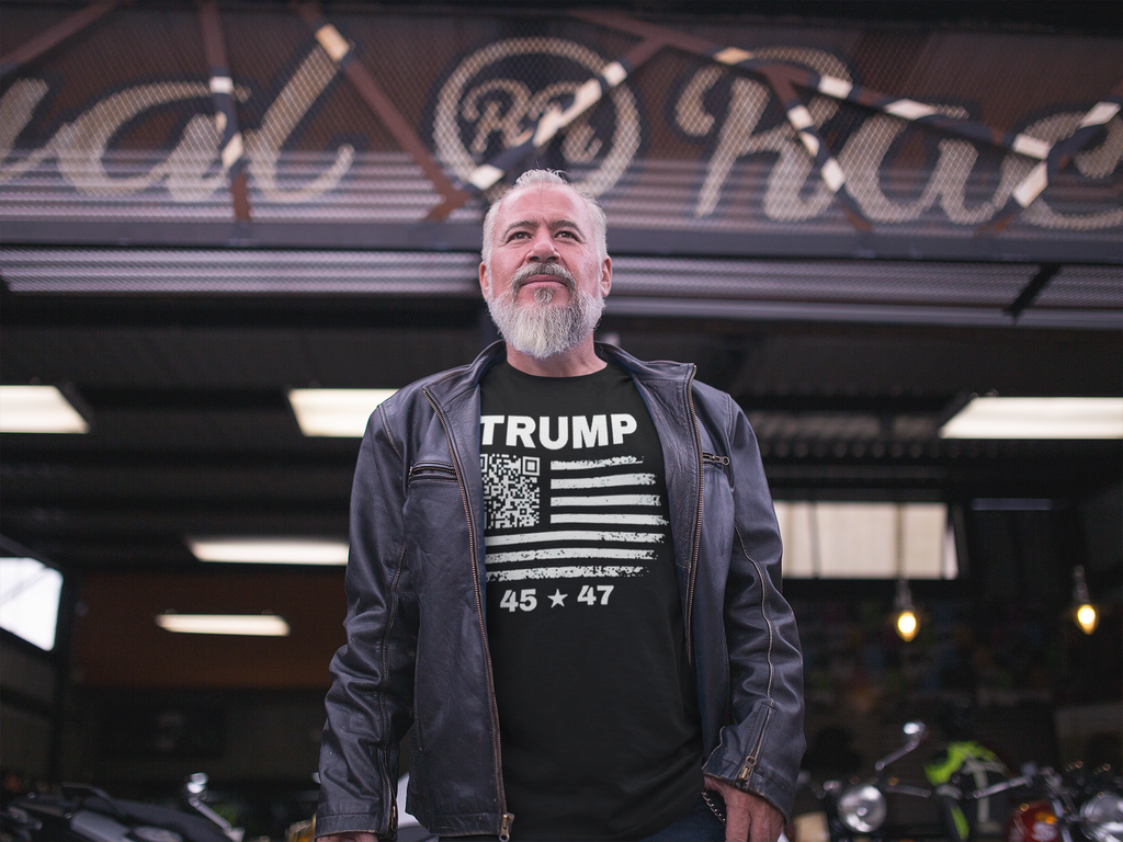 A man wearing a leather jacket and a Presidential 45 47 Trump Series graphic tee, standing in front of a bike shop.
