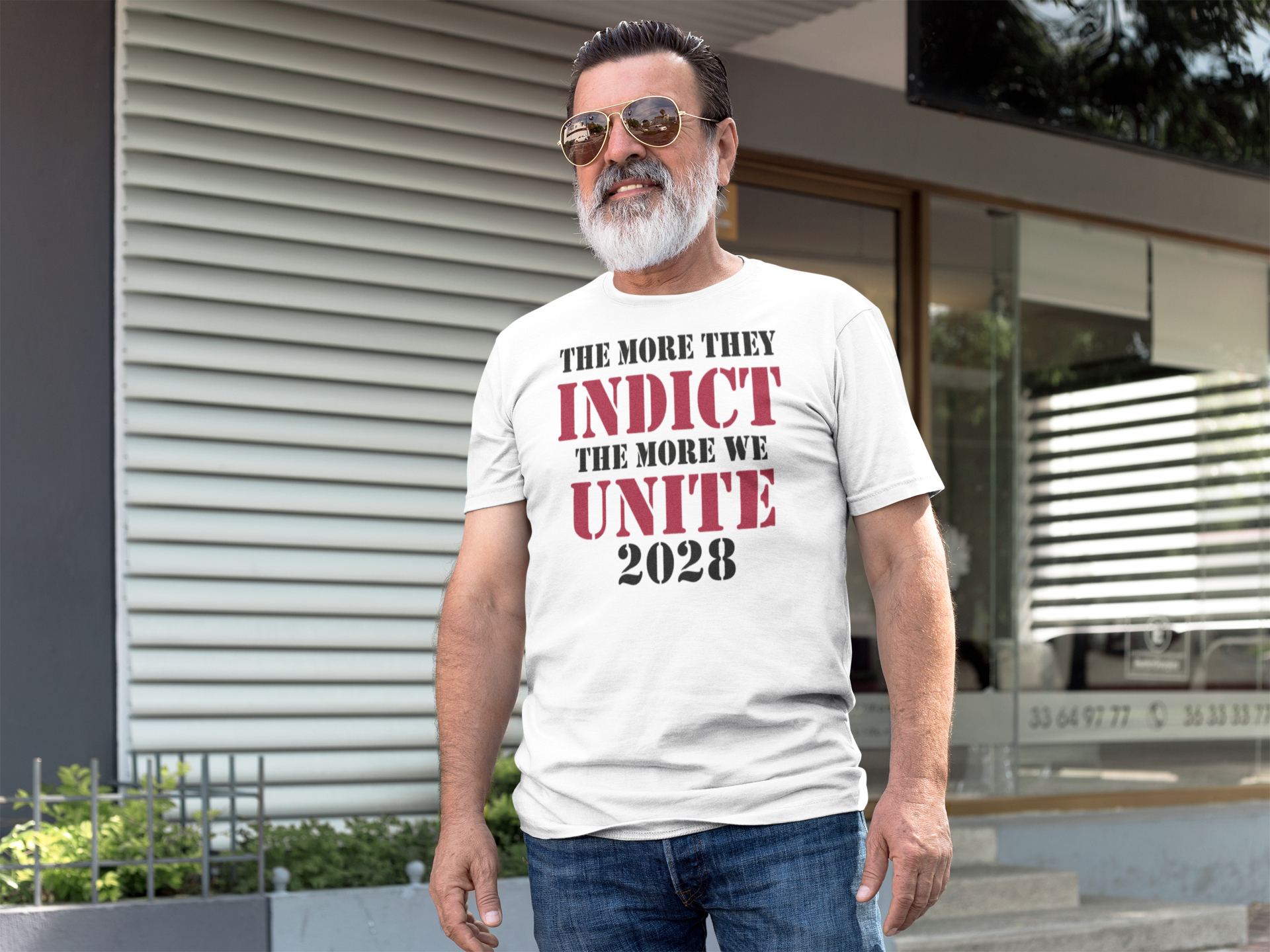 The More They Indict The More We Unite 2028 Blk Ltrs t-shirt worn by a man outdoors, showcasing strong political message.