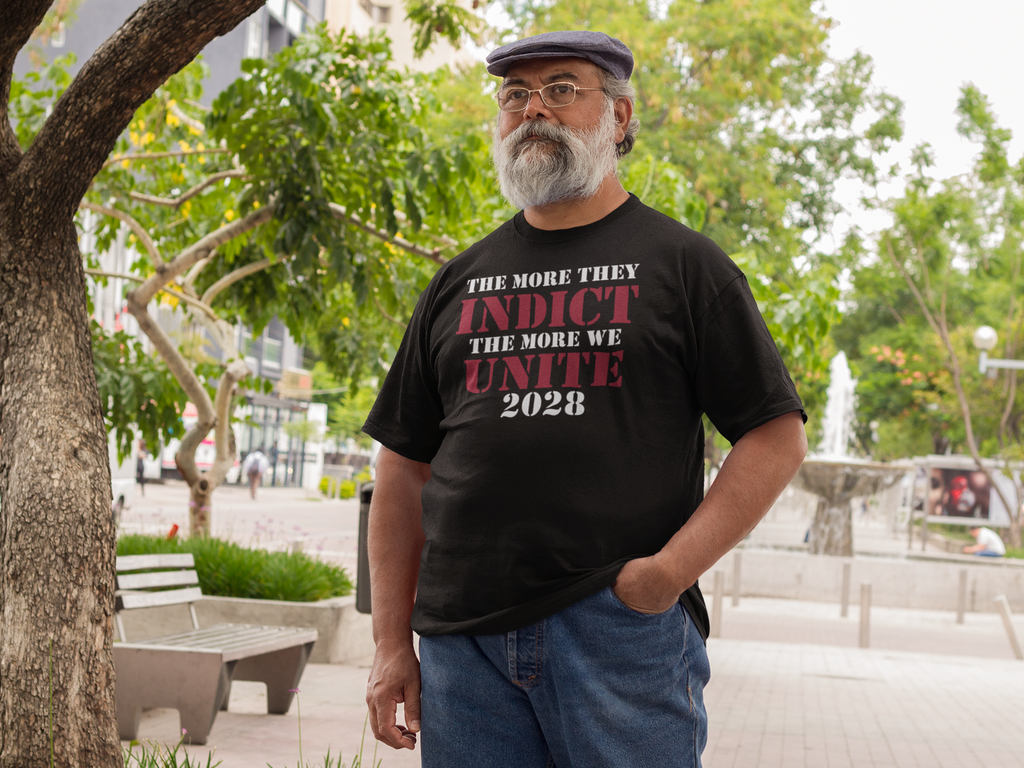 Man wearing a black t-shirt with the phrase The More They Indict The More We Unite 2028 Wht Ltrs in a park.