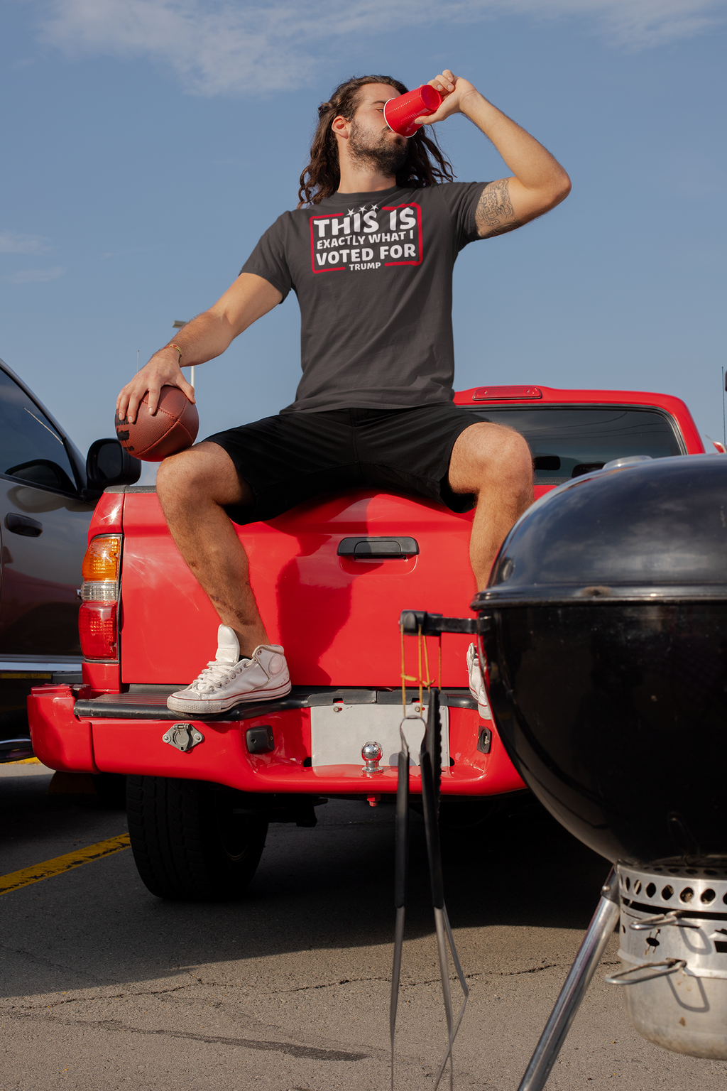 Man wearing 'This Is Exactly What I Voted For' shirt, sitting on a red truck, enjoying a drink.