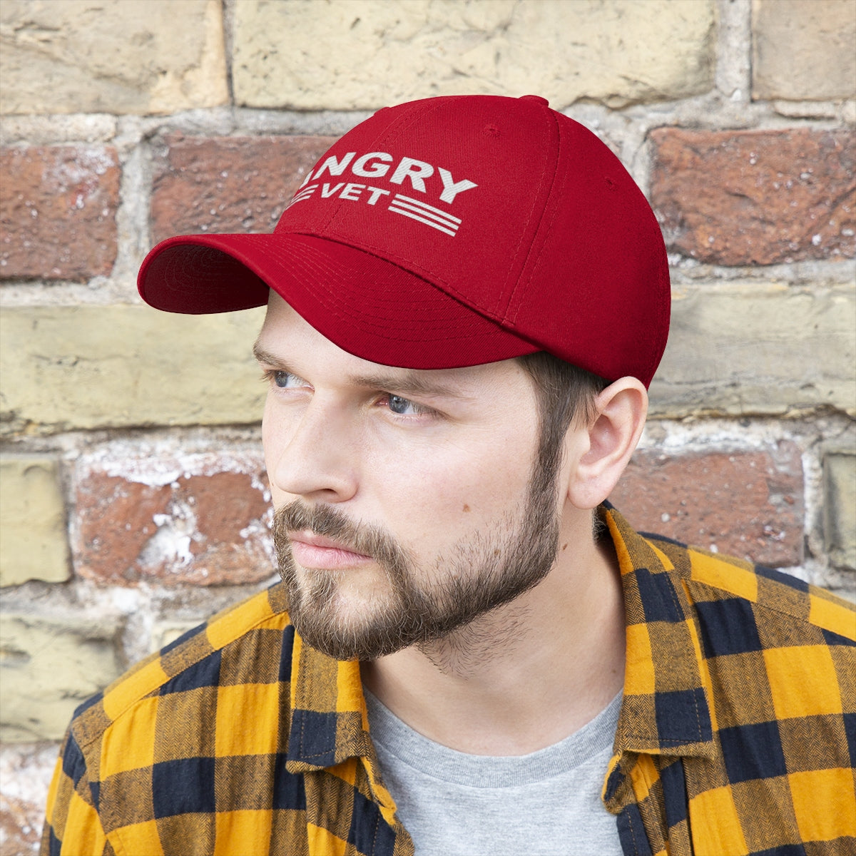 Angry Vet Twill Cap Veteran Pride Graphic Hat worn by man with beard and plaid shirt against brick wall.