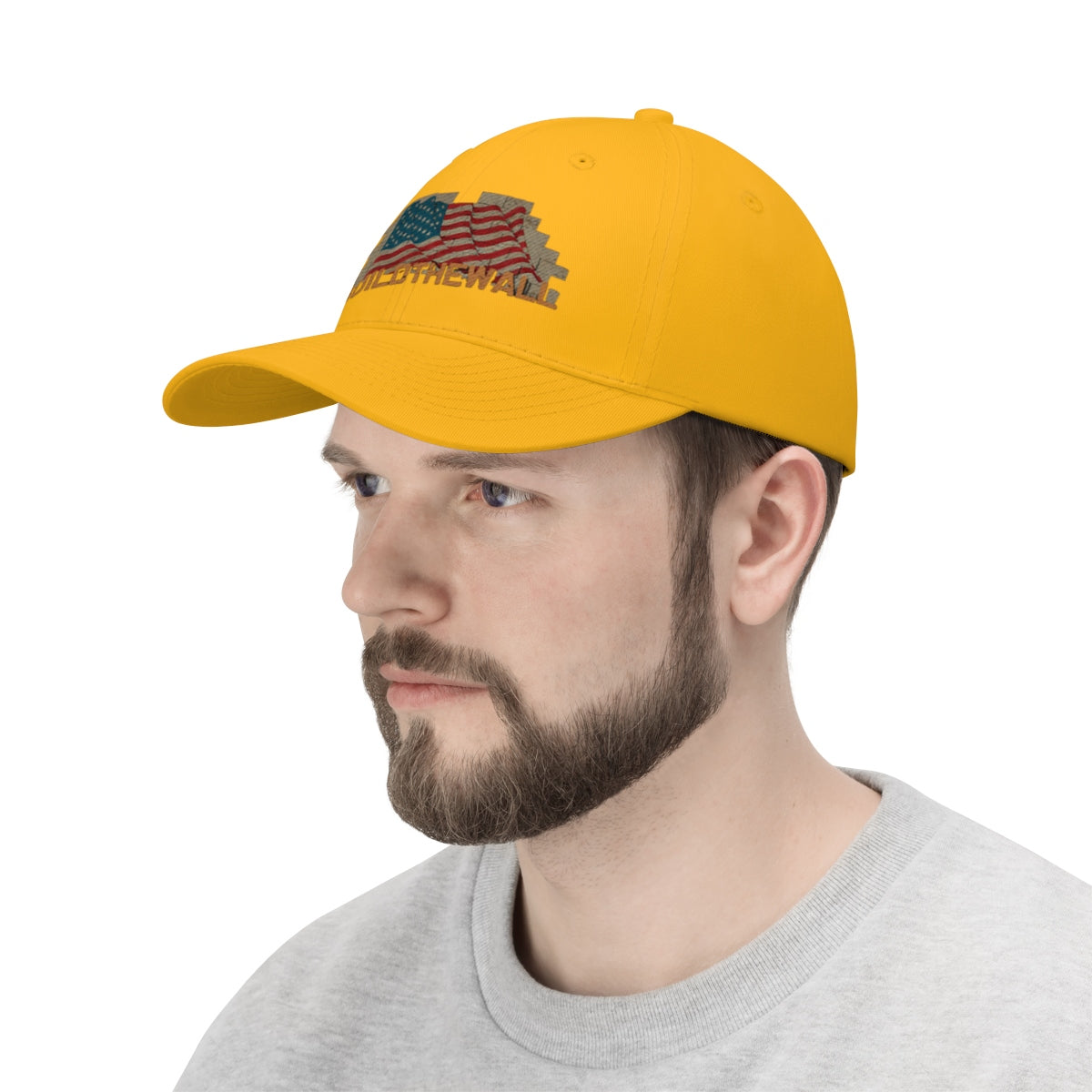 Build The Wall On American Flag Twill Cap worn by a man with a beard, featuring patriotic design and yellow color.
