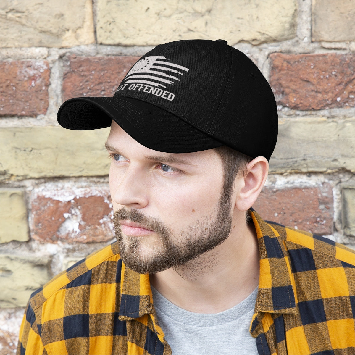 Man wearing an Embroidered Not Offended Adjustable Twill Cap against a brick wall.
