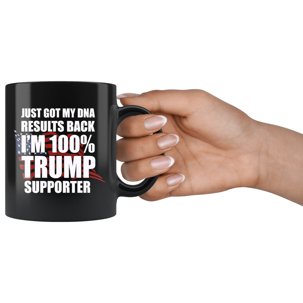 Black mug with text: Just Got DNA Results I Am 100 Percent Trump Supporter, held by a hand against a white background.