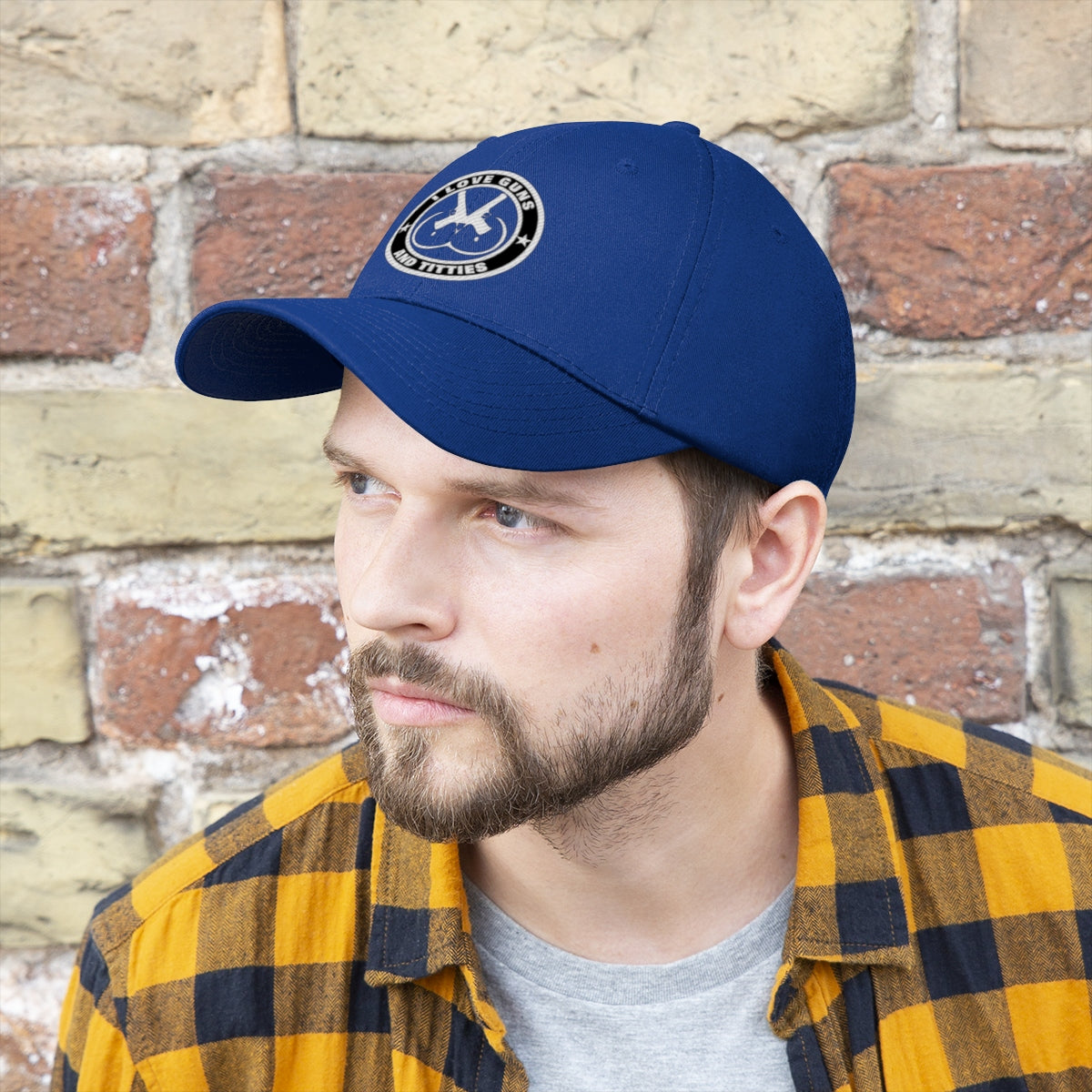 I Love Guns And Titties Twill Cap displayed on a man in front of a brick wall.